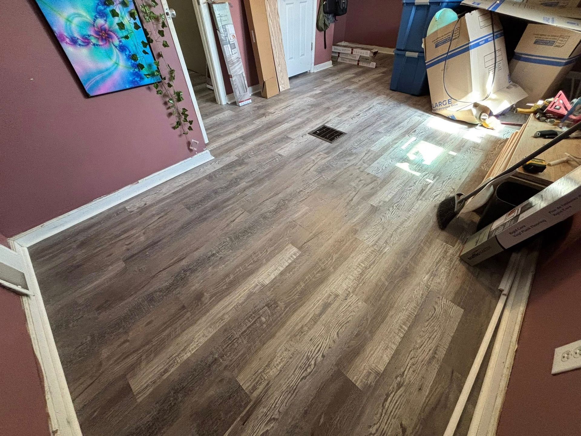 Partially renovated room with wood-look flooring, pink walls, and tools and boxes along the right side.