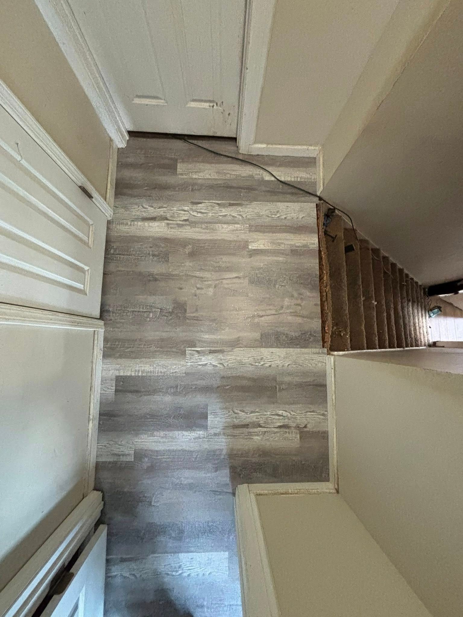 Top-down view of a narrow stair landing with gray wood flooring and white walls.