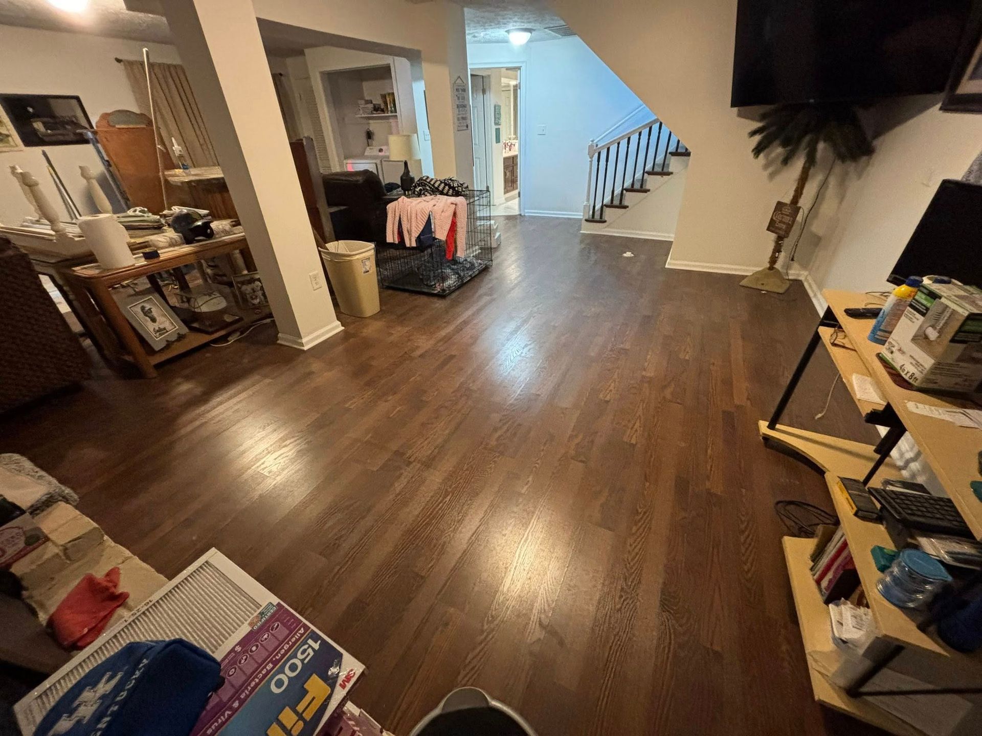 Living room with dark wood floors, TV, staircase, and cluttered shelves near the right wall