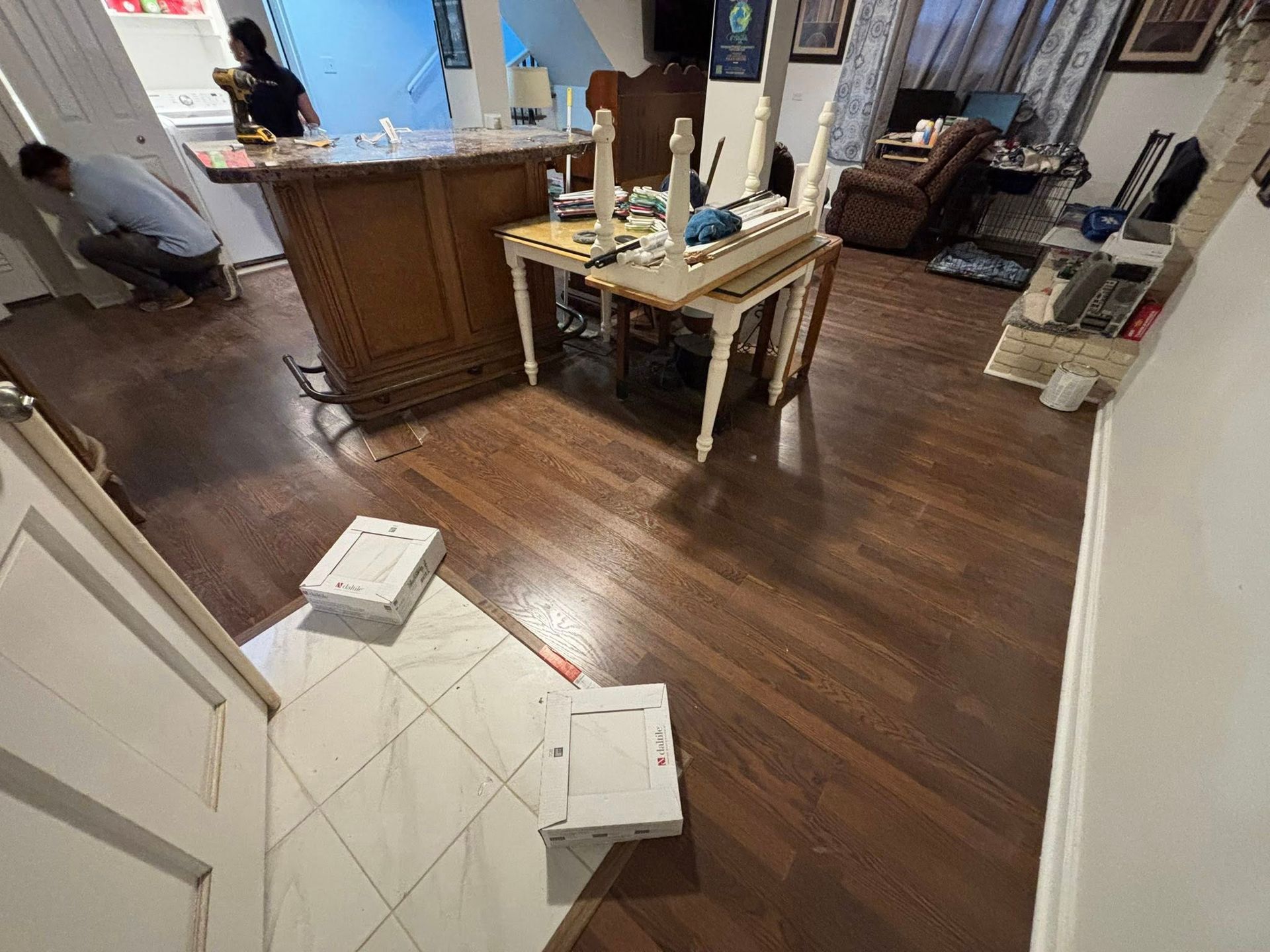 Living room with hardwood floor, tiled entryway, kitchen island, and cardboard boxes on the floor