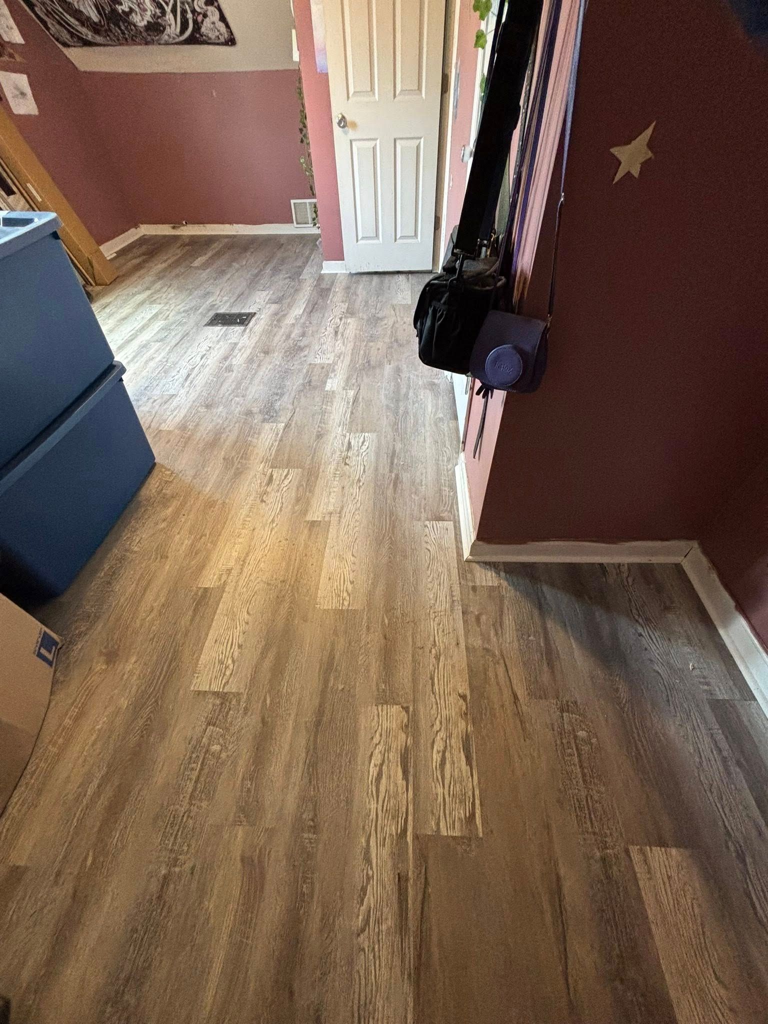 Empty bedroom with wood flooring, maroon walls, white door, and a dresser along the left wall.