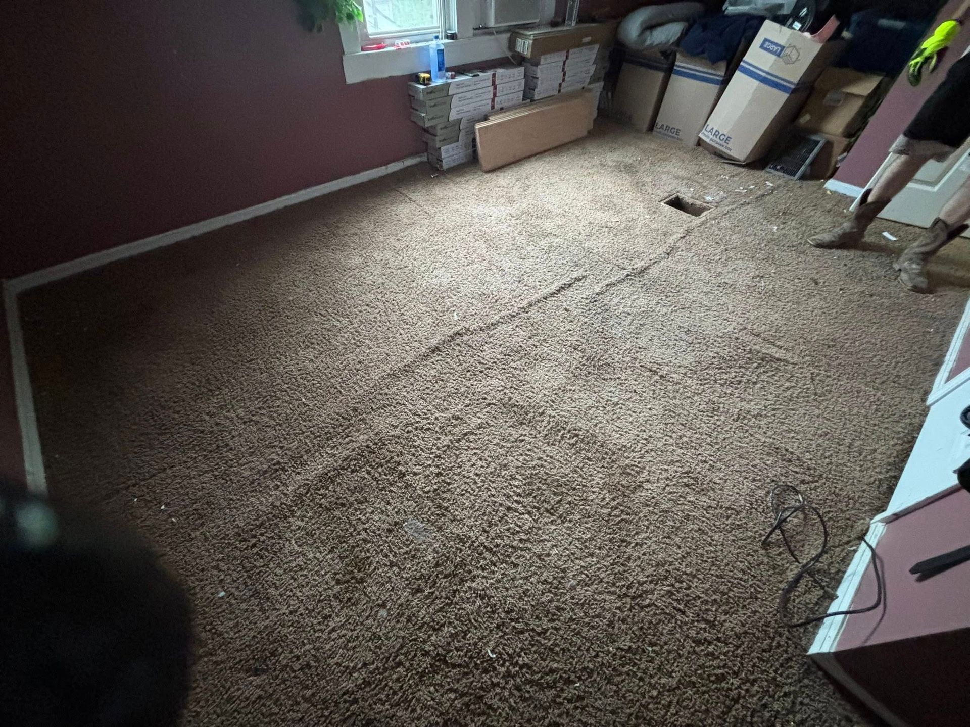 Messy bedroom with a carpeted floor, boxes near the window, and a person standing at the right edge.