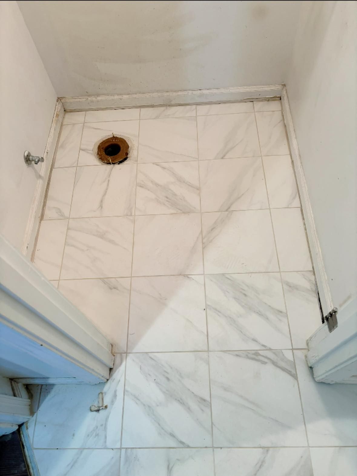 Small tiled utility room floor with a drain and white walls, viewed from a doorway.