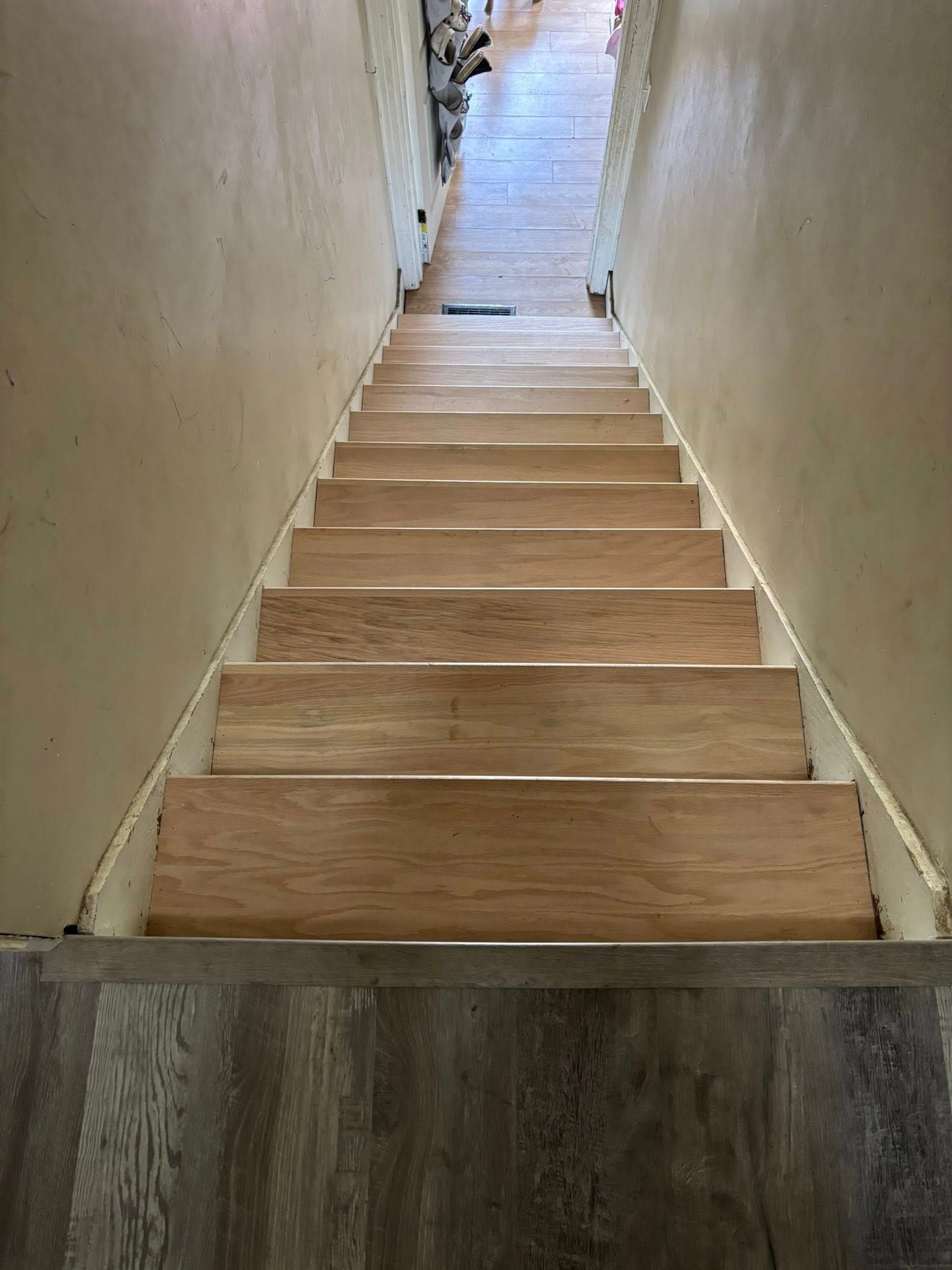 Narrow indoor wooden staircase leading up between beige walls to a bright landing