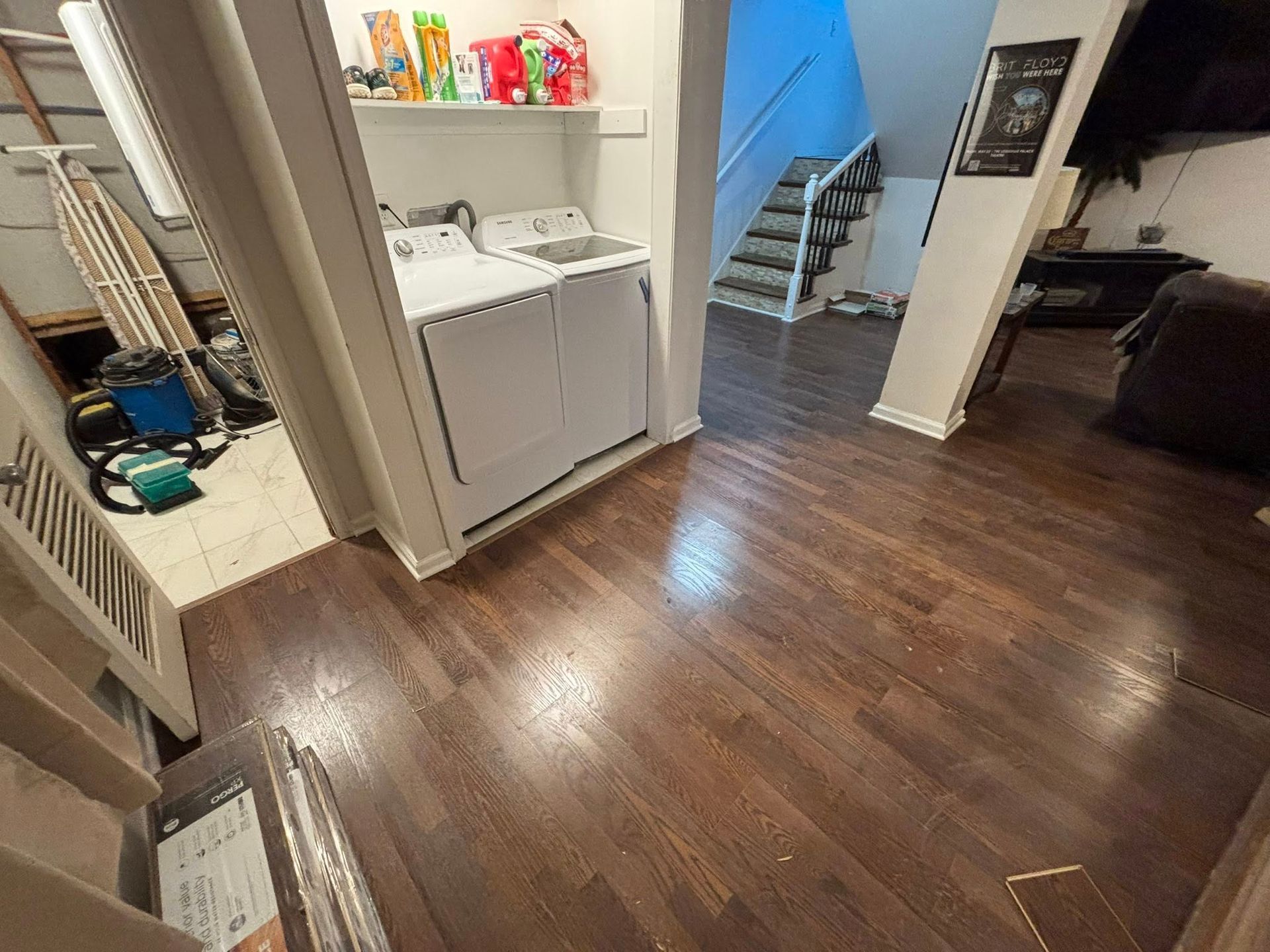 Open living area with dark wood floors, laundry nook, stairs, and a desk in the background.