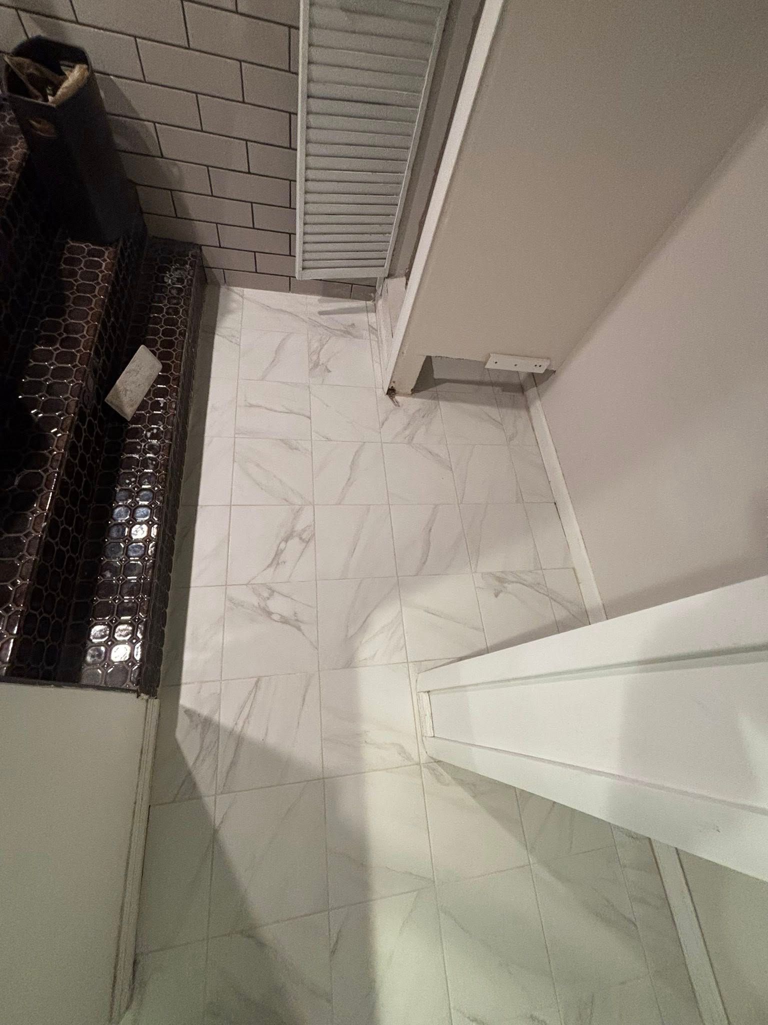 Narrow indoor hallway with light tile floor, white walls, and a patterned metal railing on the left.