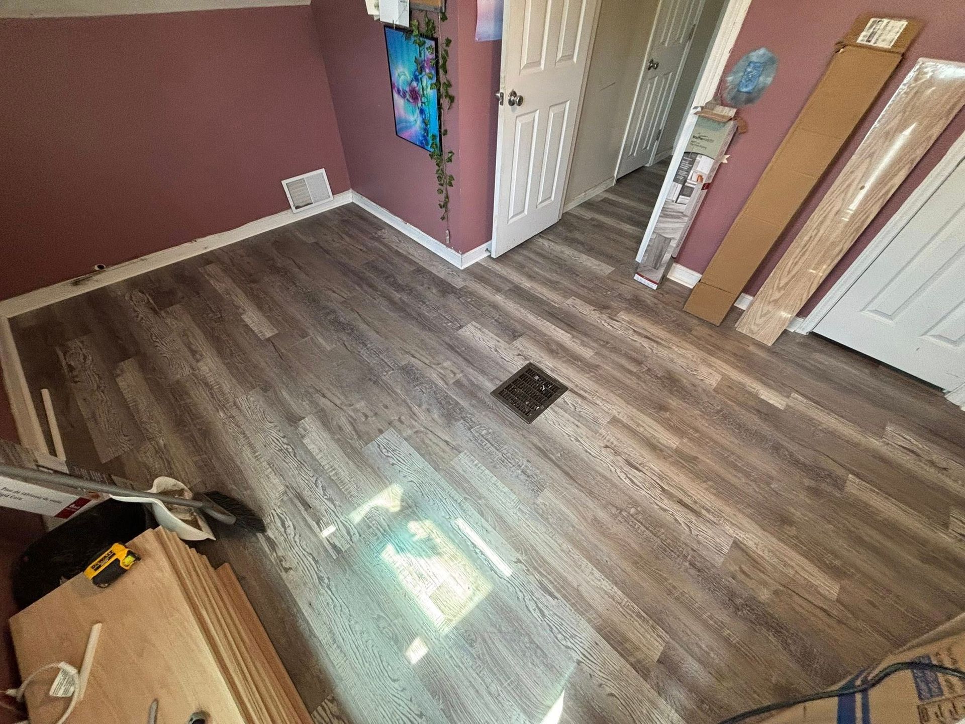 Empty room with wood-look flooring, pink walls, and a white door near a hallway.