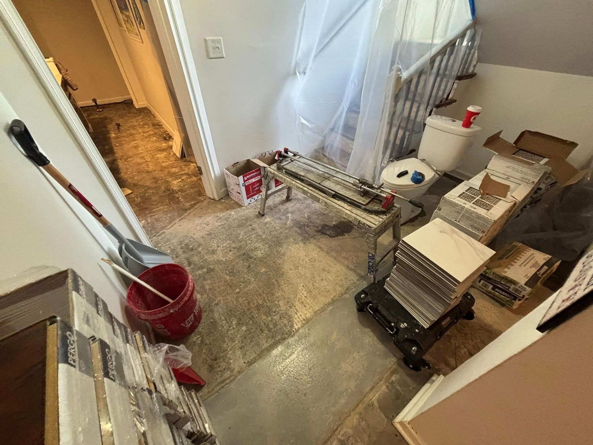 Cluttered stairwell with cleaning supplies, boxes, and construction materials on the landing and steps