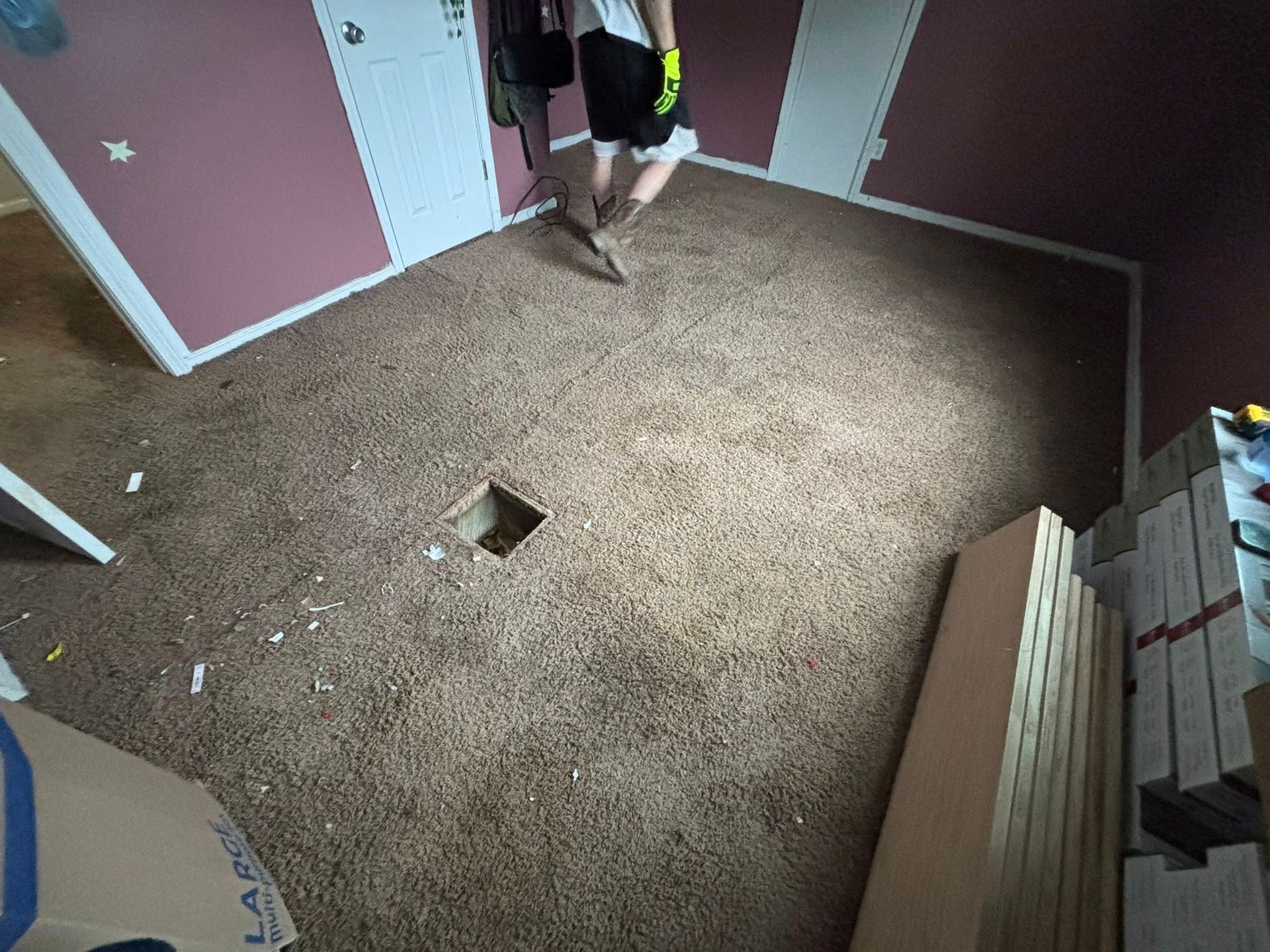 Carpeted room with a square hole in the floor and a person standing near the door.