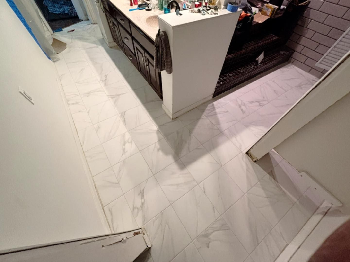 White tiled hallway entrance leading to a countertop and dark cabinets in a tiled interior hallway