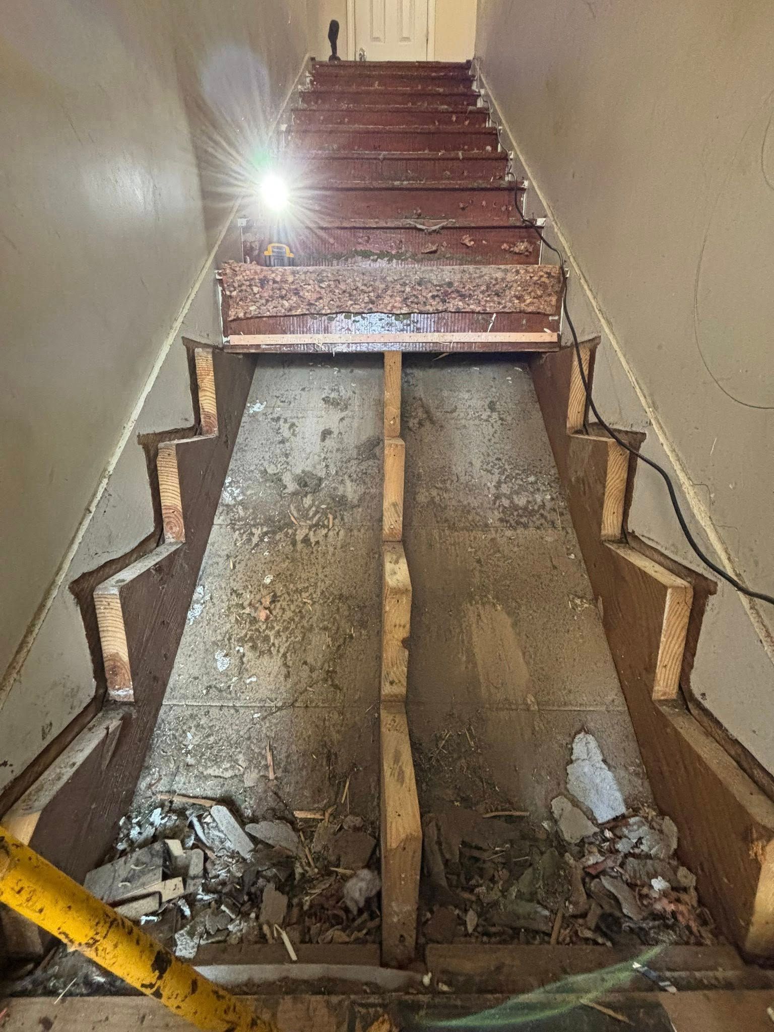 Collapsed staircase with exposed debris and two damaged wooden supports in a narrow hallway.