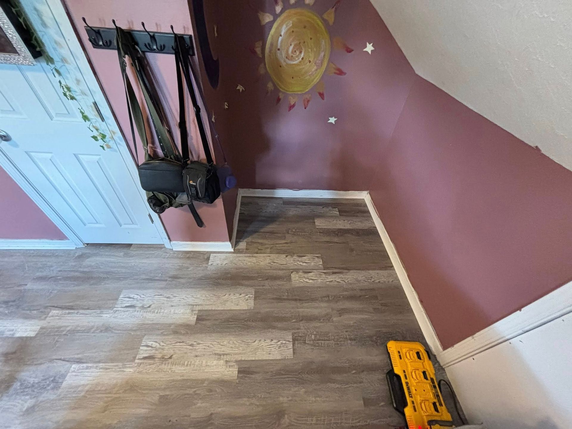 Small attic room with pink walls, sloped ceiling, wood floor, and hanging clothes near a closet.