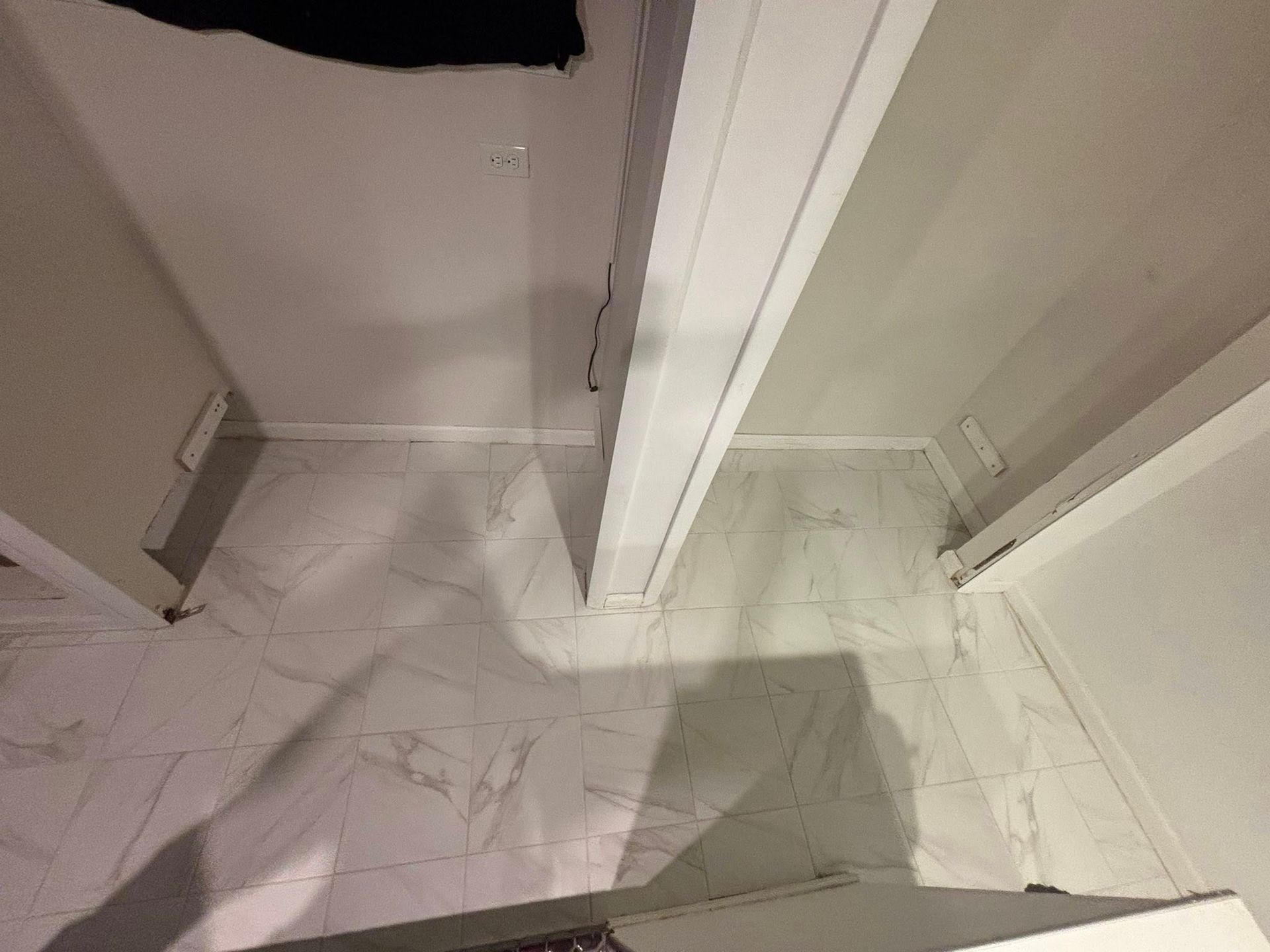 White marble-tile floor beside a shower or closet entrance, with a shadow cast across it.