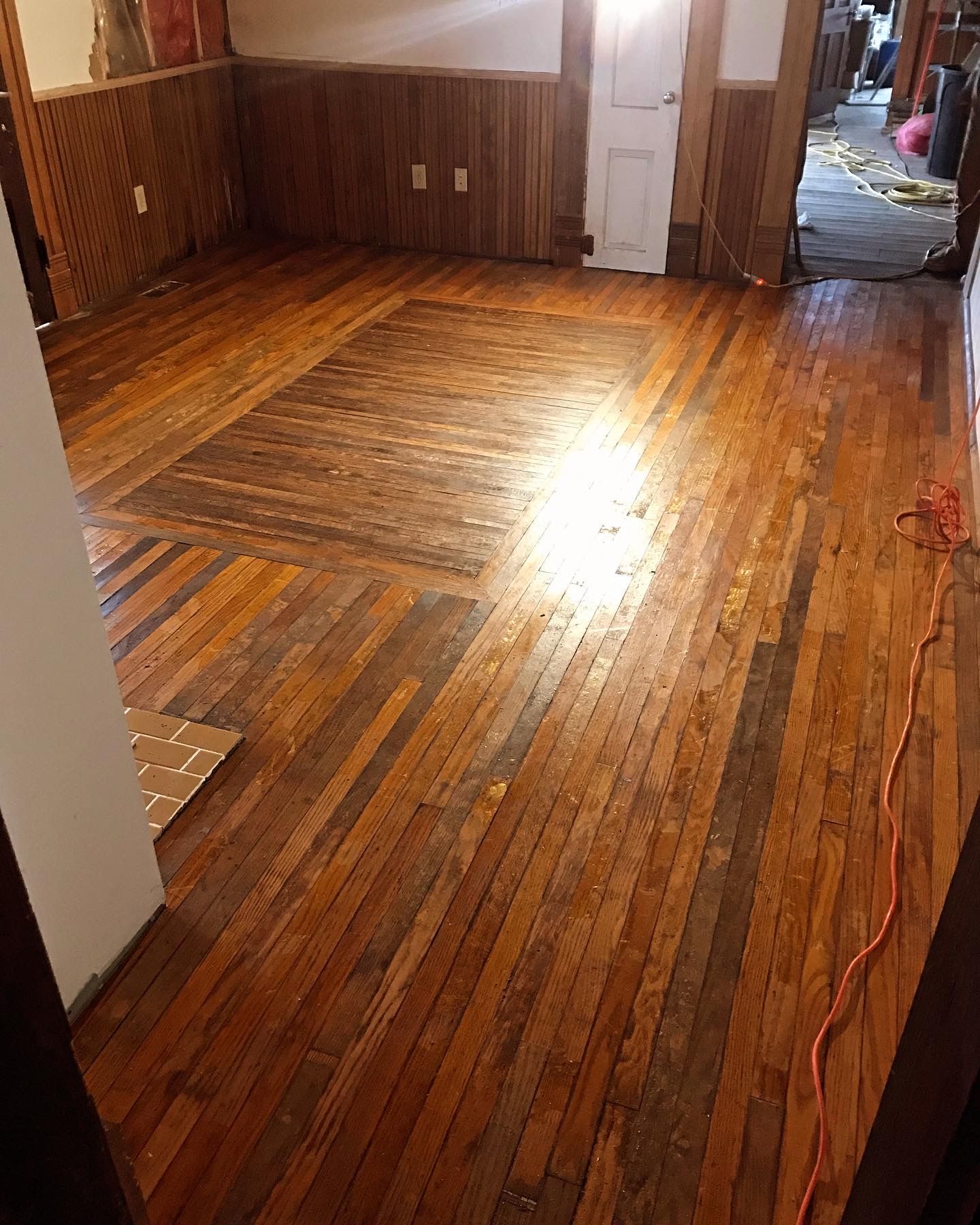 Empty room with worn wooden floors and paneling, bright sunlight reflecting near the center.