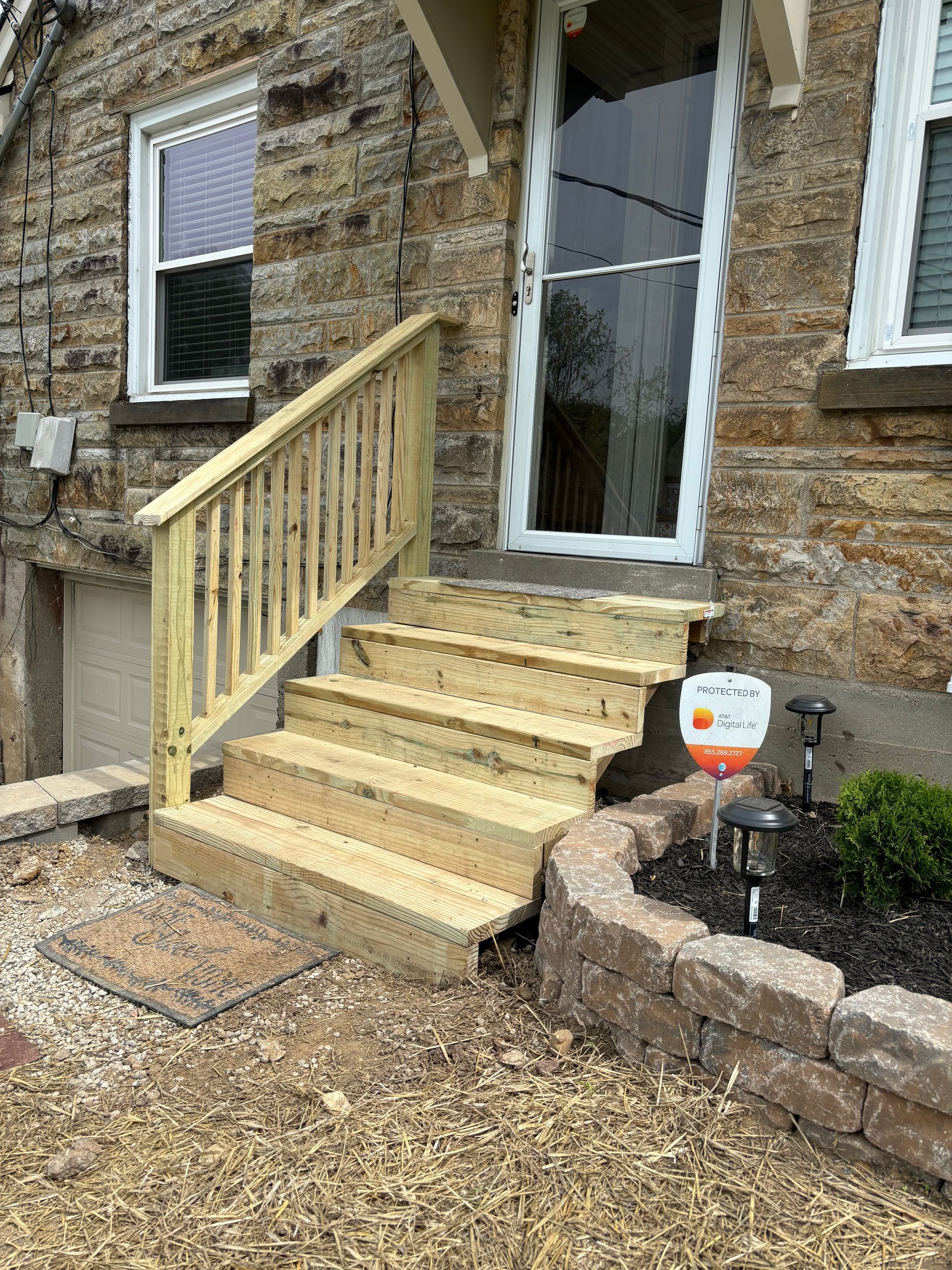 Stone house entrance with yellow porch steps, white door, and small pumpkin decoration by the walkway