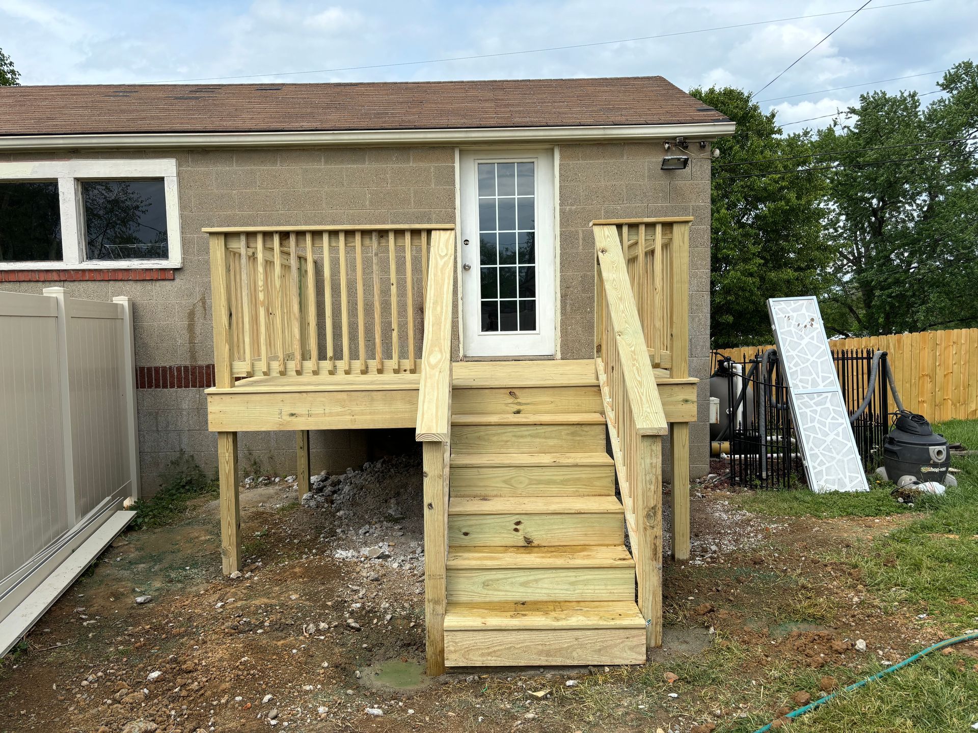Wooden front deck and stairs added to a small house, with railings and a glass door.