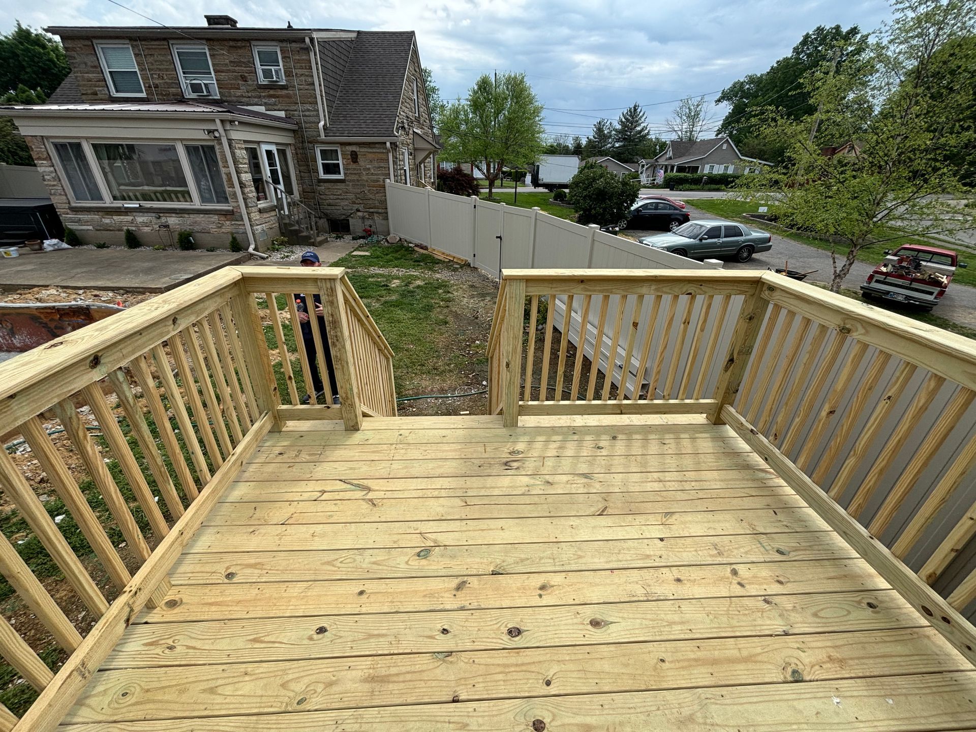 Wooden deck with railings overlooking a stone house and street below