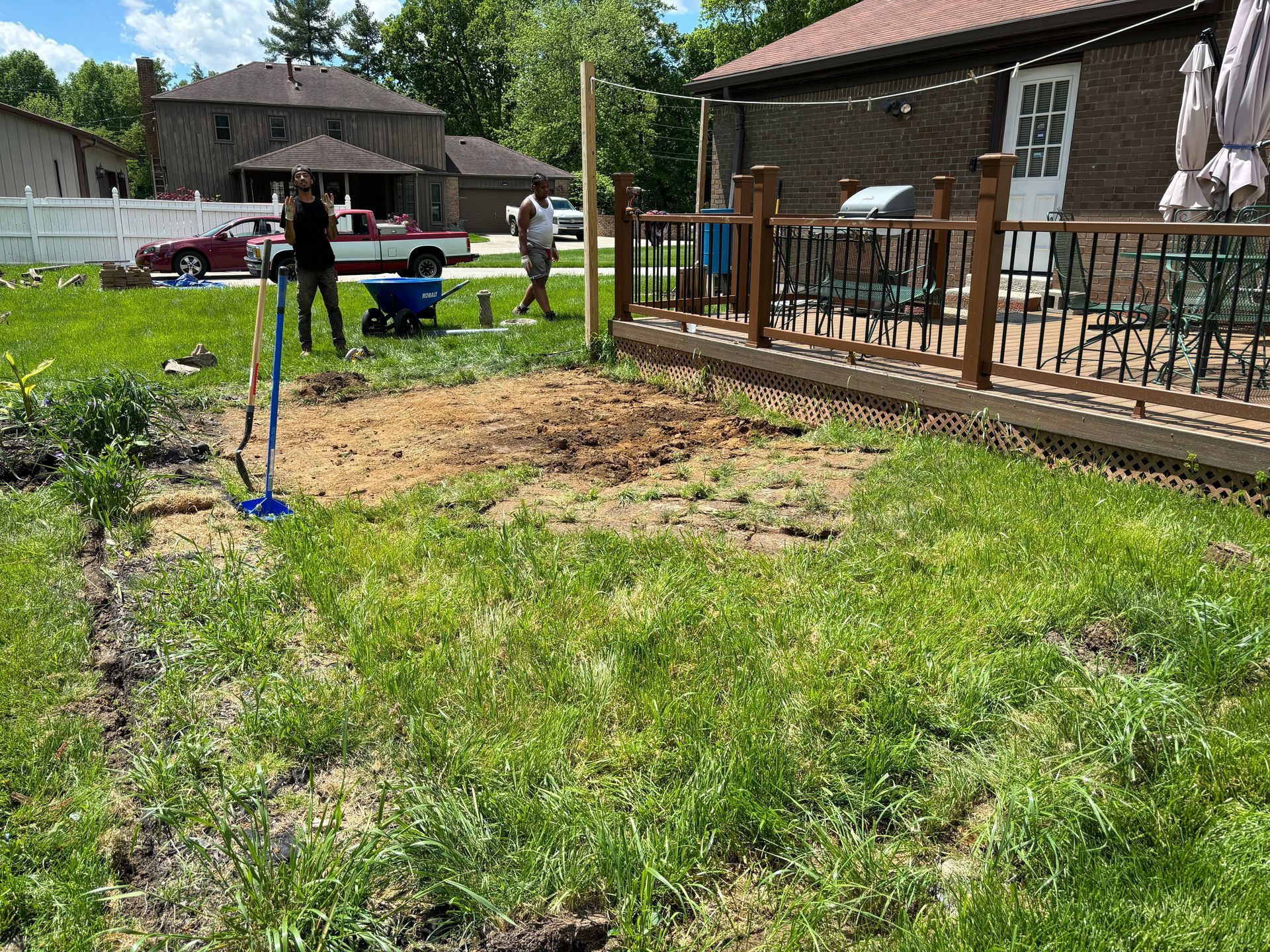 Backyard with grass and a wooden deck; people stand near a house and a red canopy in the background