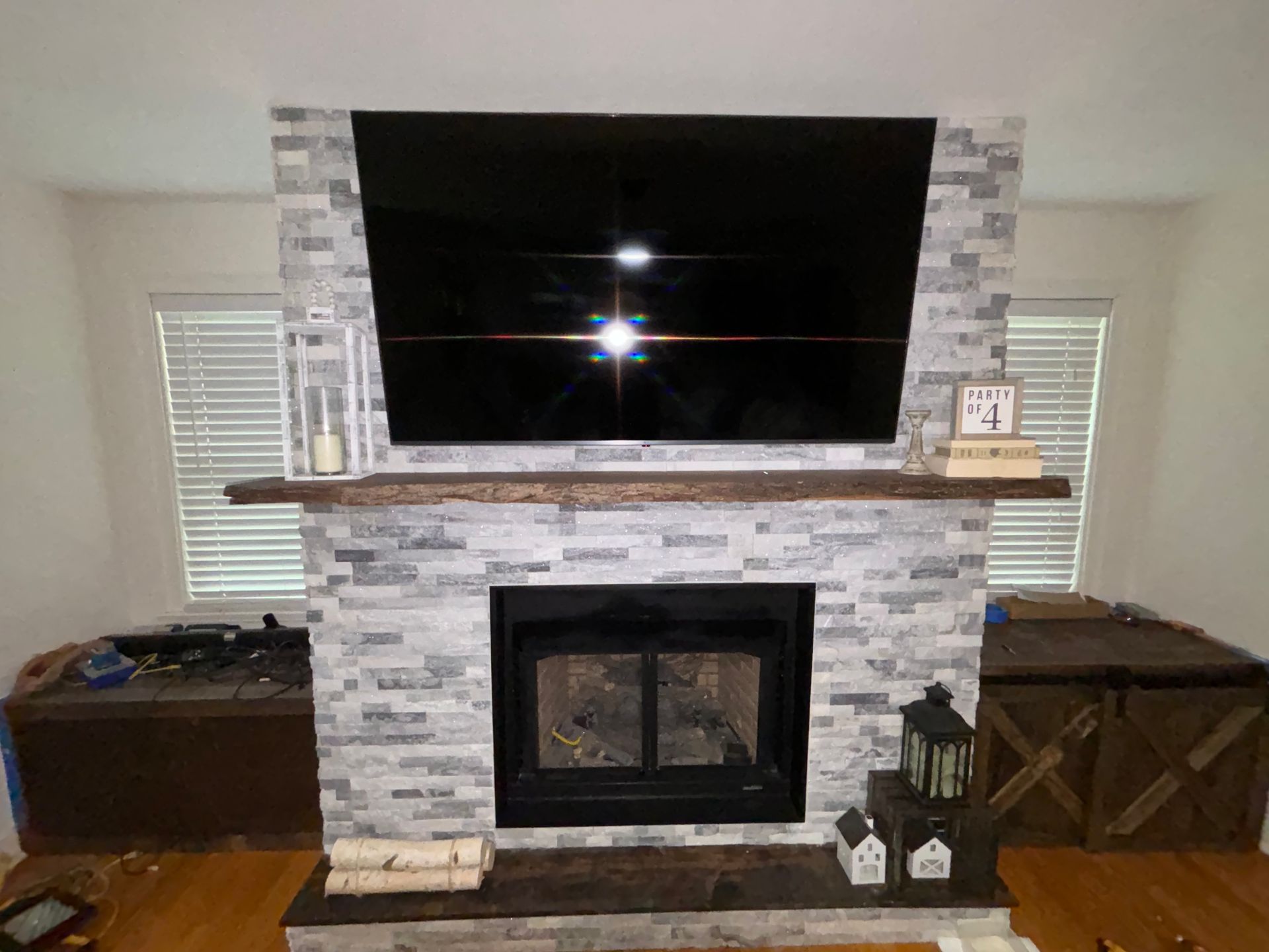 Living room fireplace with mounted TV, stone surround, wooden mantel, and windows on both sides
