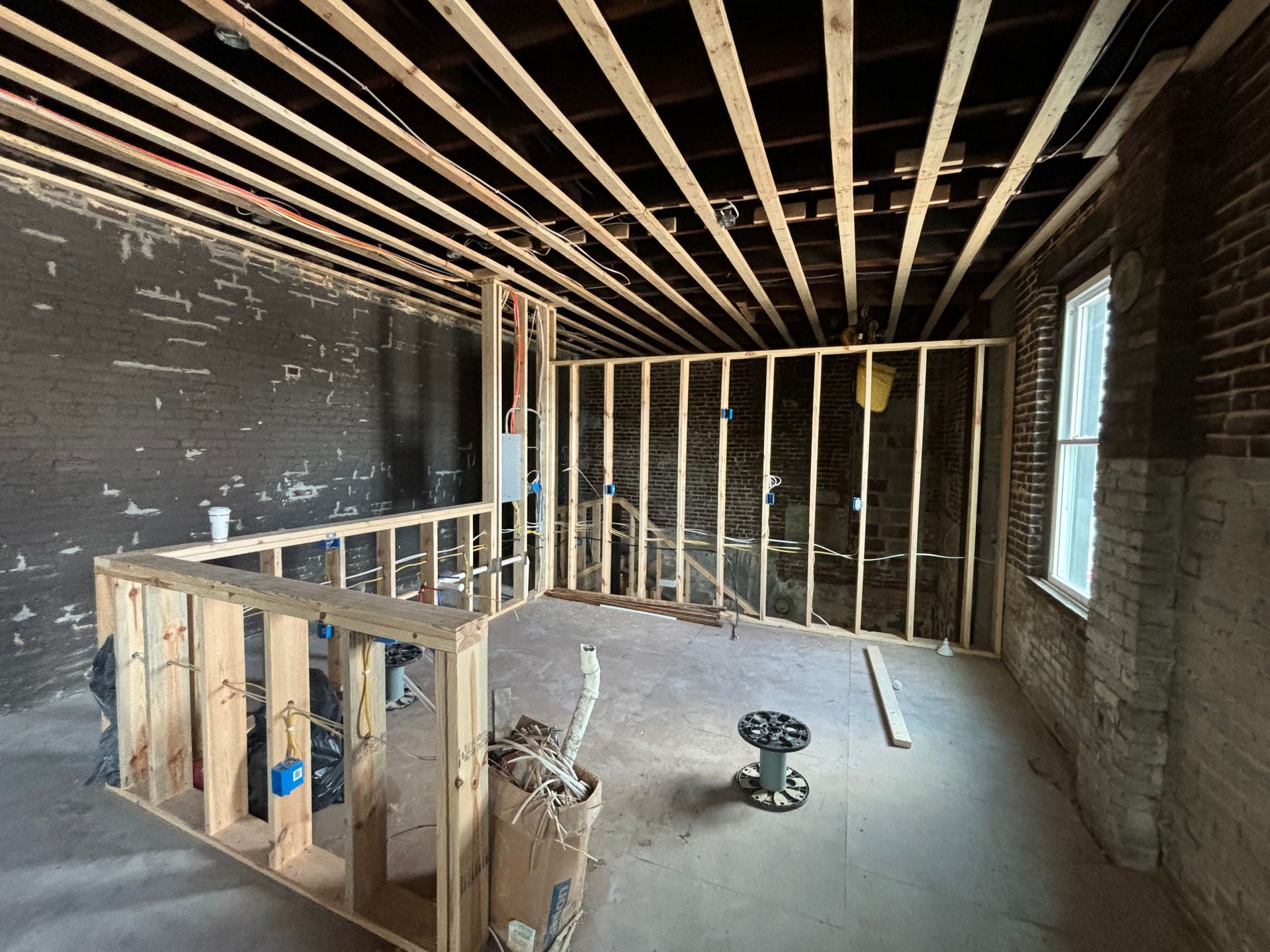 Unfinished room with exposed studs, brick walls, a window, and construction tools on the floor.