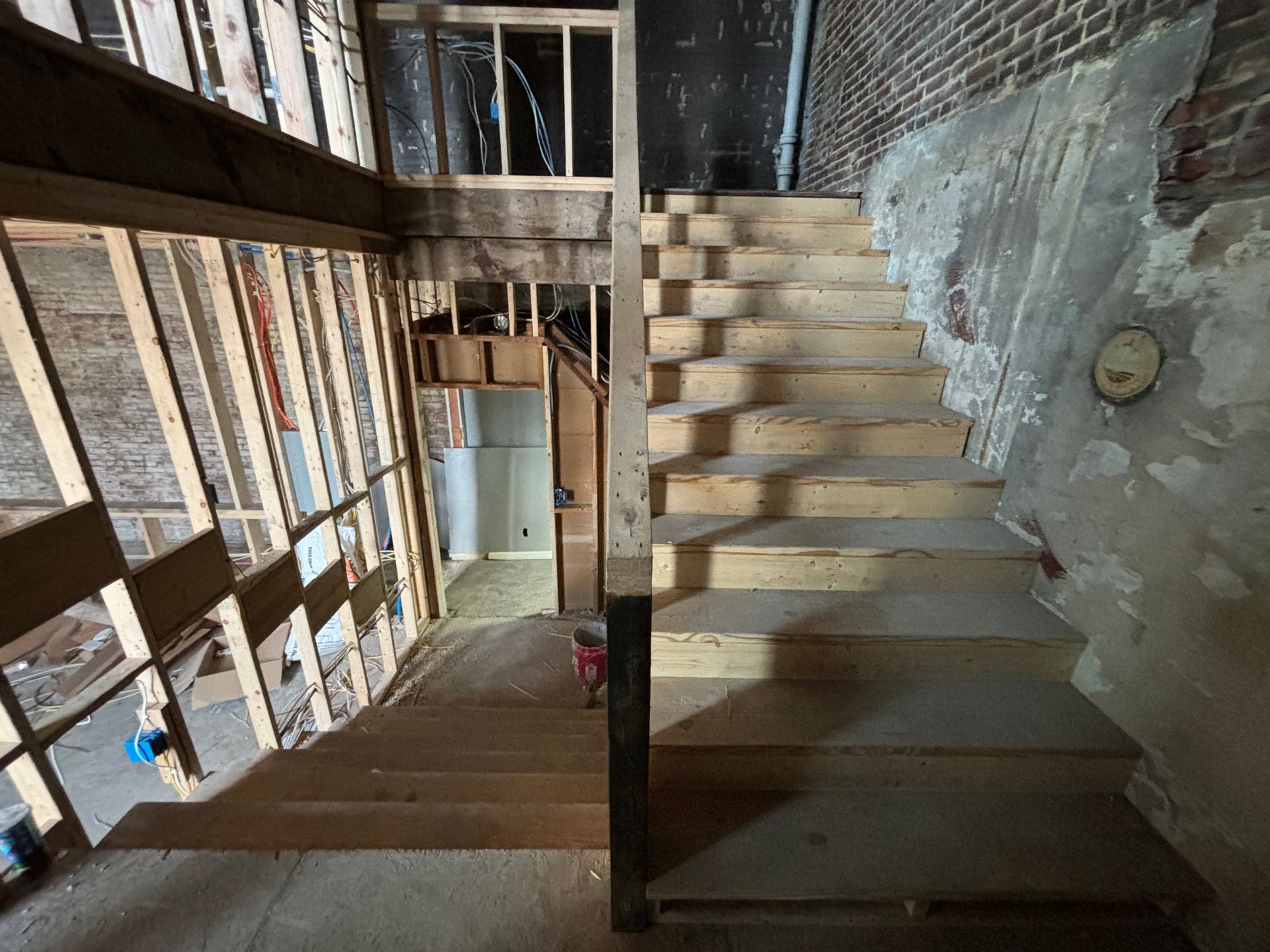 Old stairwell with exposed brick walls, wooden steps, and a central support post in a narrow interior space
