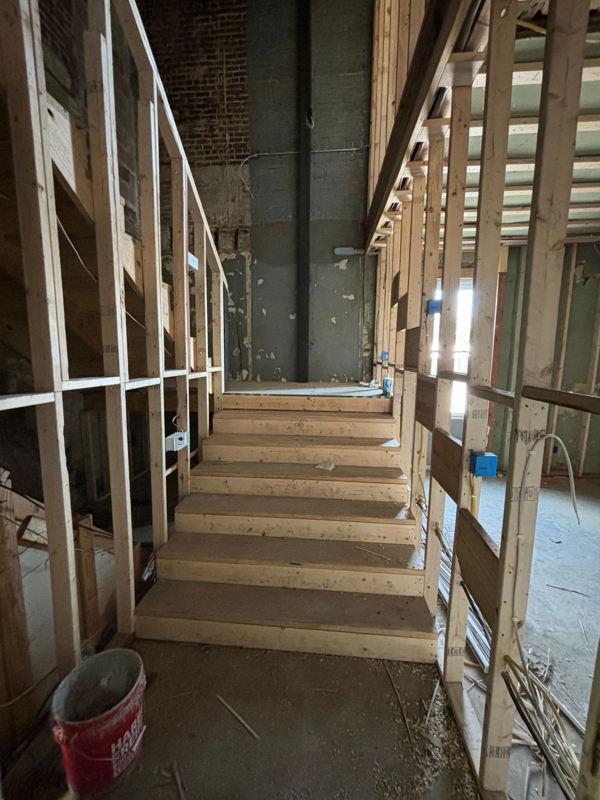 Unfinished indoor staircase under construction, framed by exposed wooden studs and concrete walls.