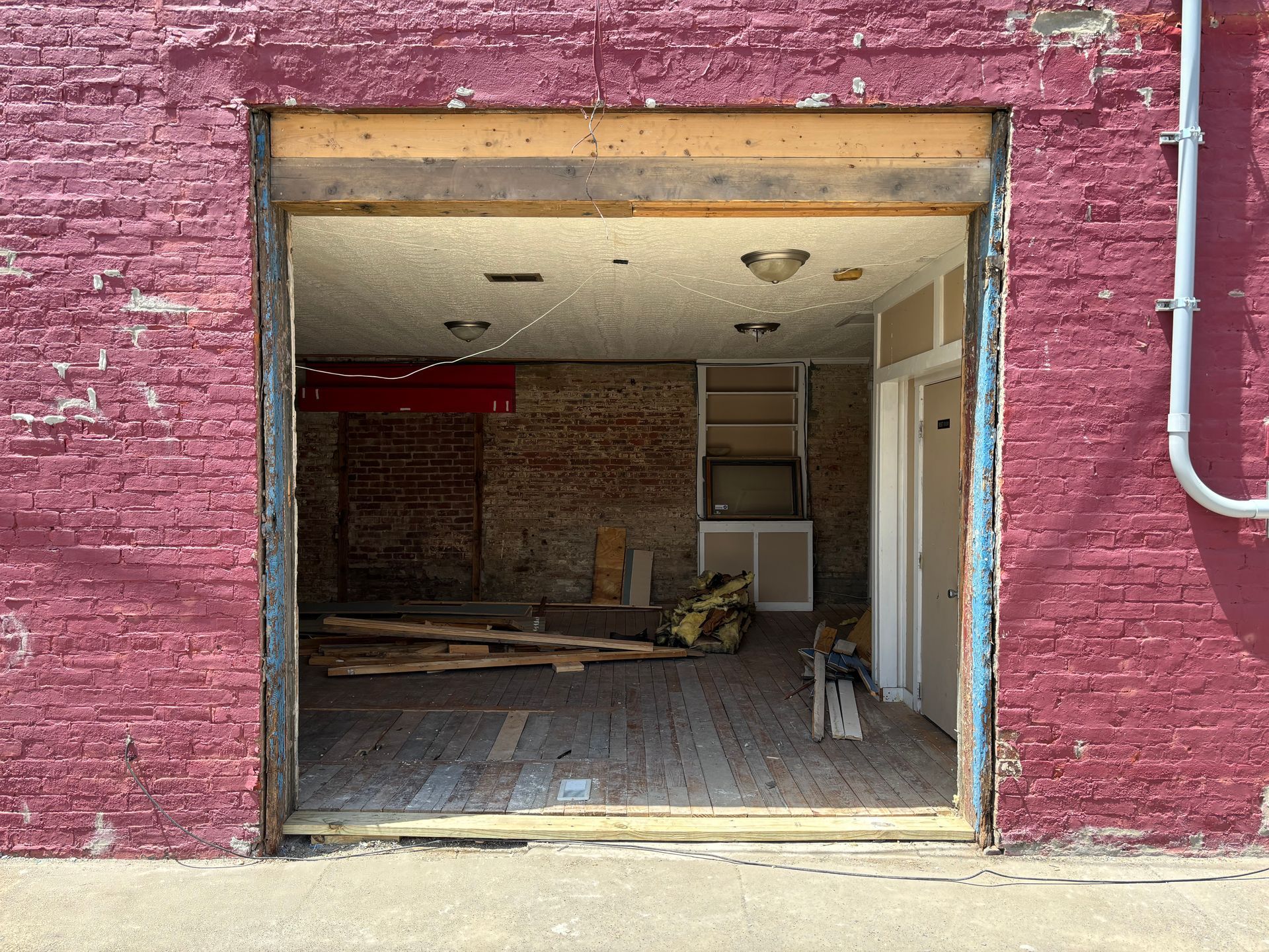 Empty brick storefront with a wide open doorway and debris inside