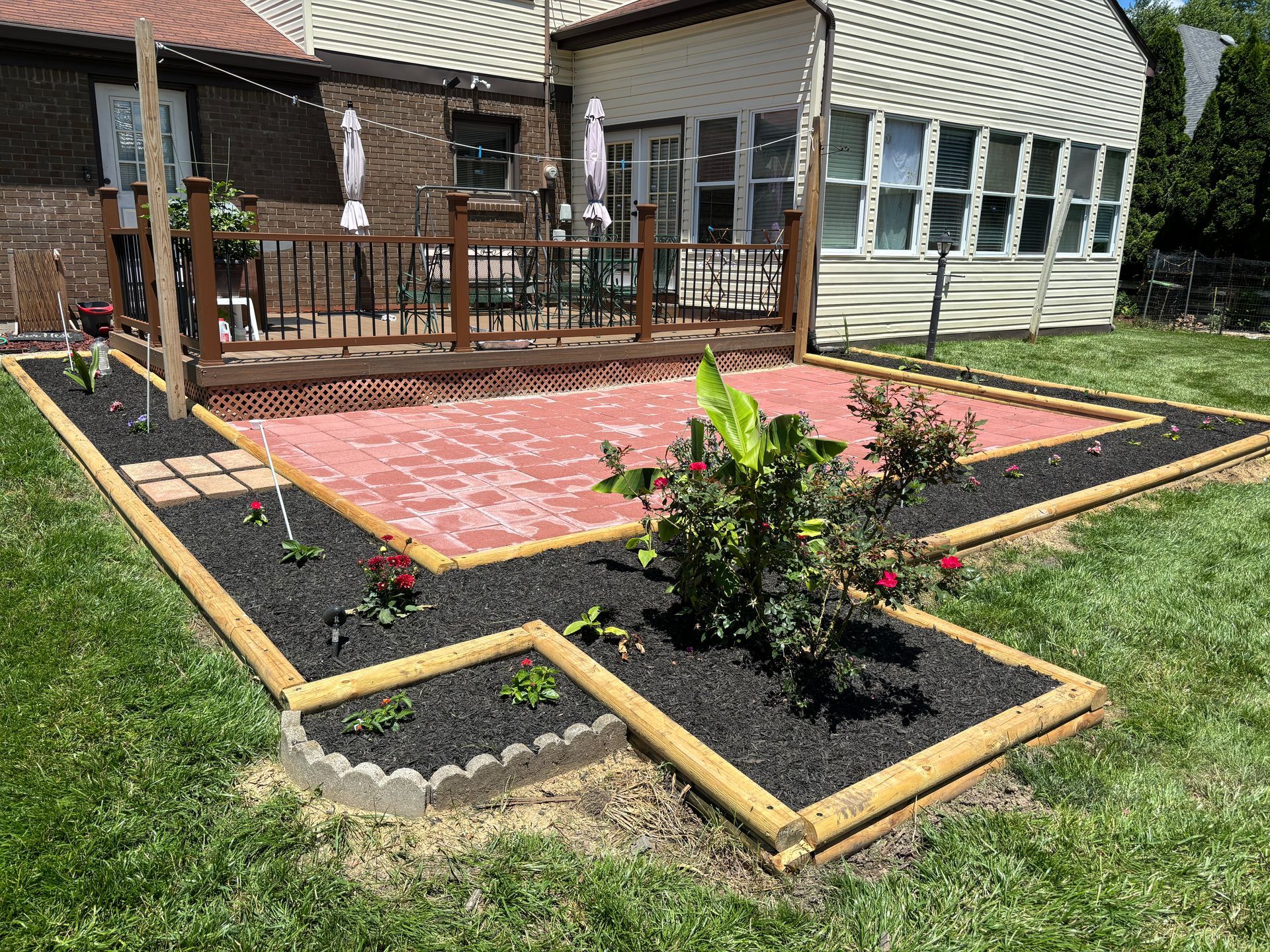 Backyard patio with raised flower beds, wooden deck, and a brick house exterior
