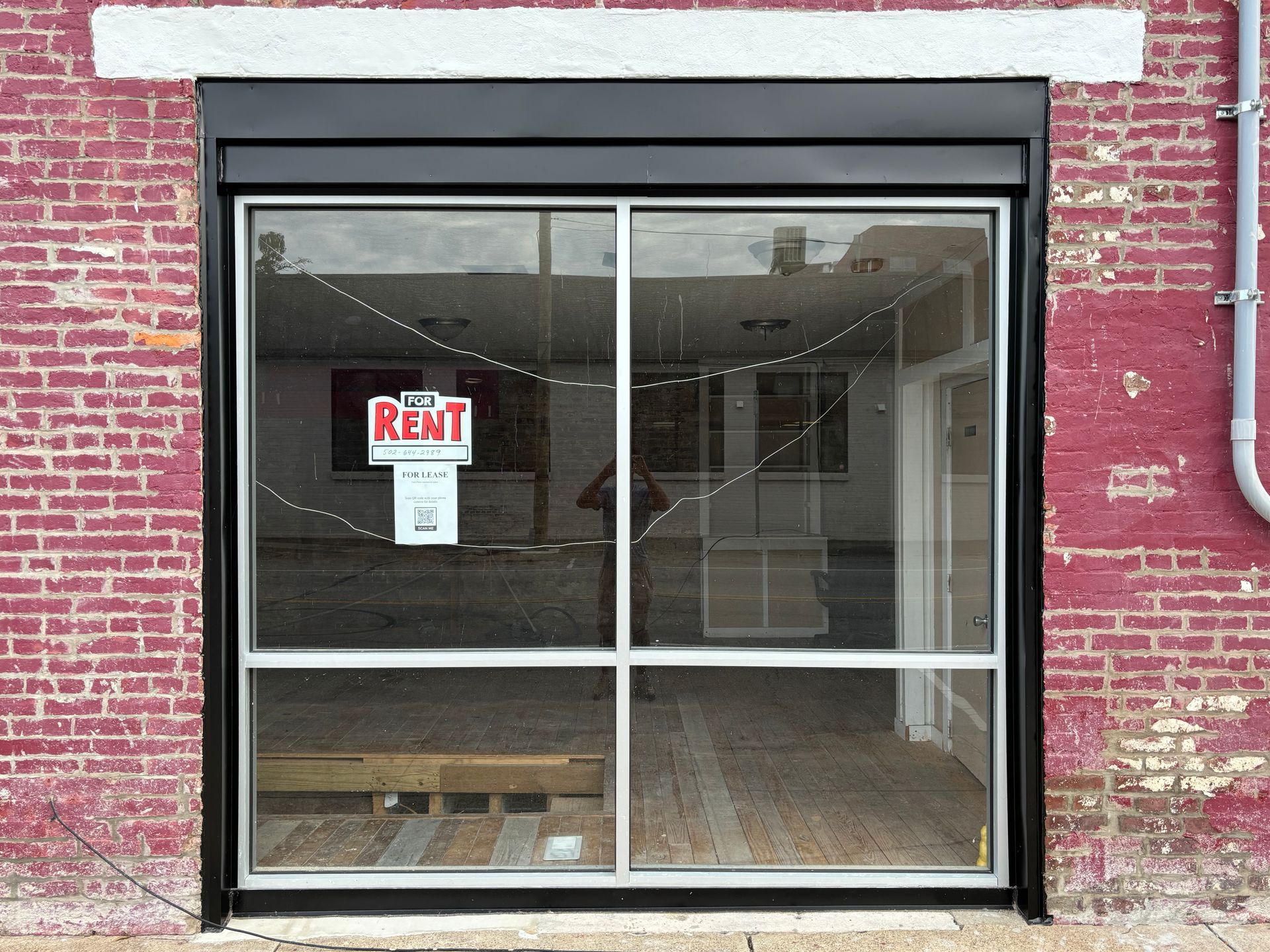 Vacant storefront with red brick exterior and a “Rent” sign in the window