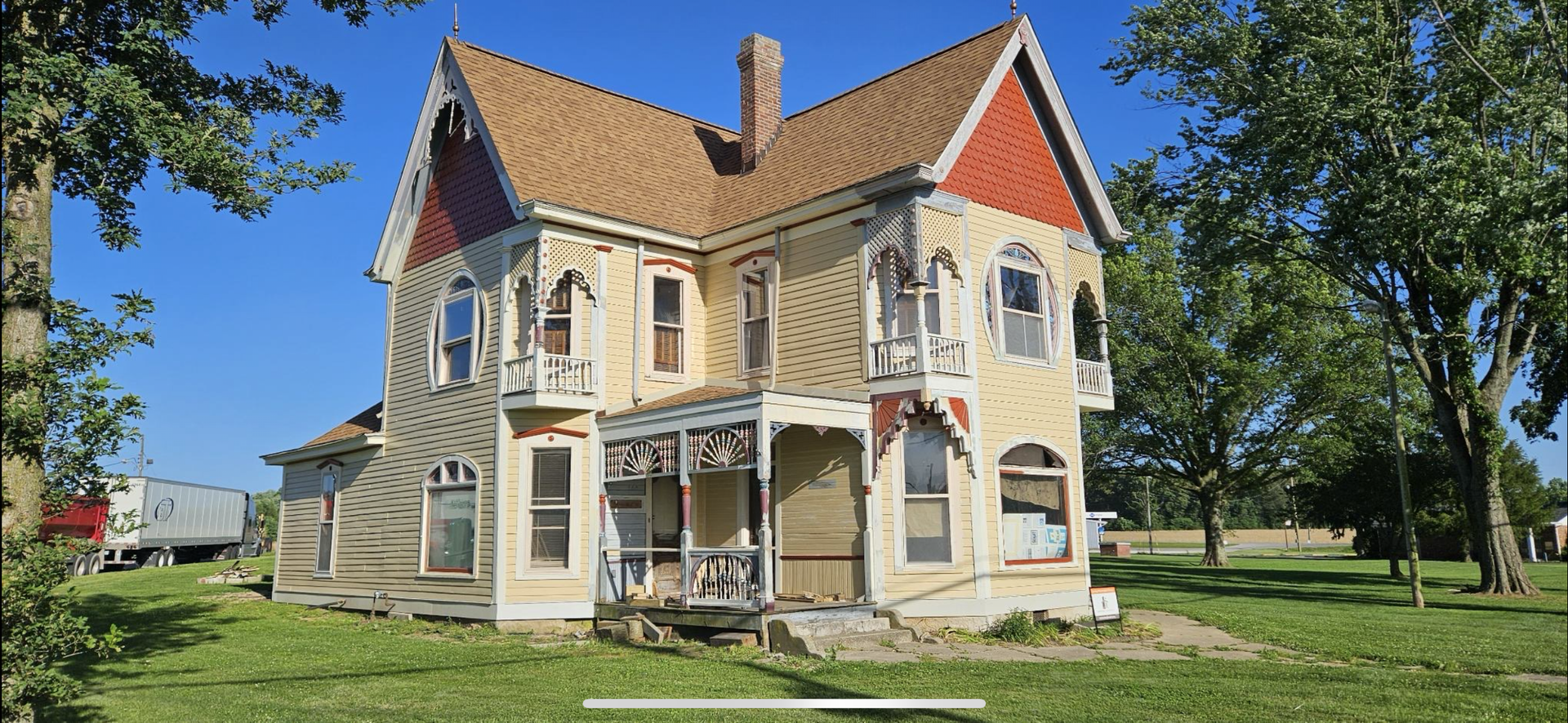 Victorian-style house with cream siding, red roof trim, and a front porch on a sunny lawn