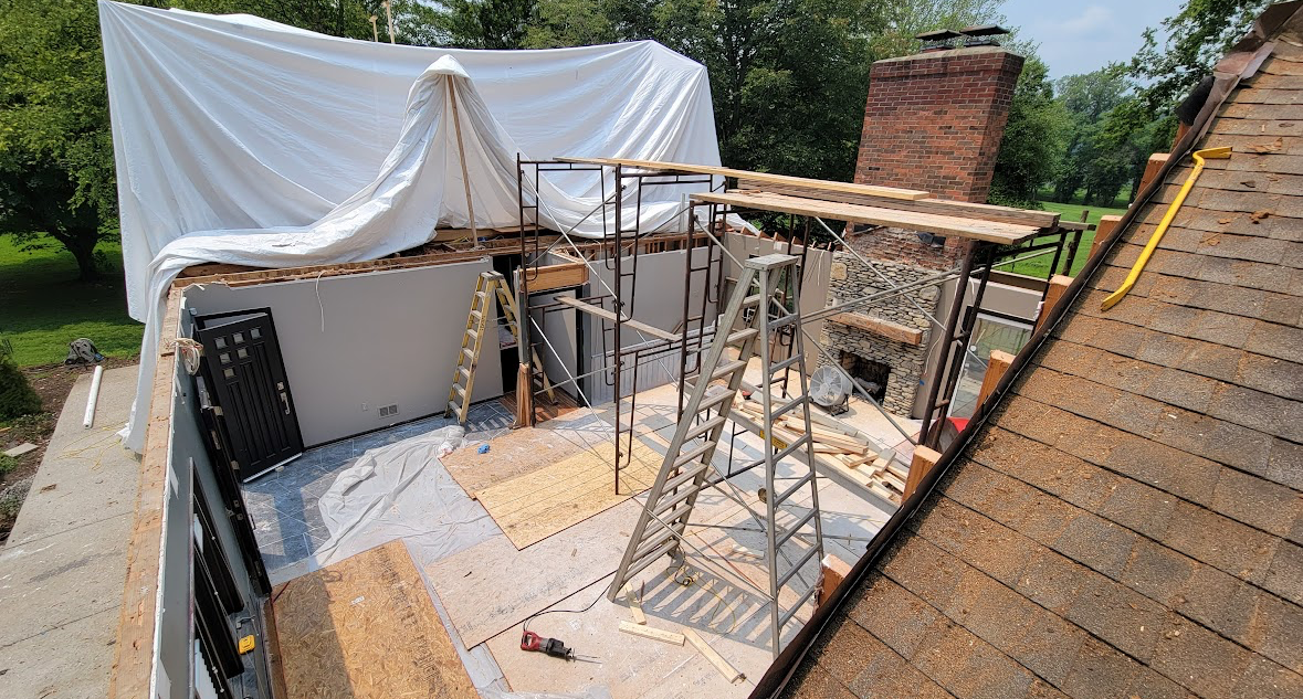 Rooftop construction with scaffolding, plywood, and a white tarp draped over the work area.