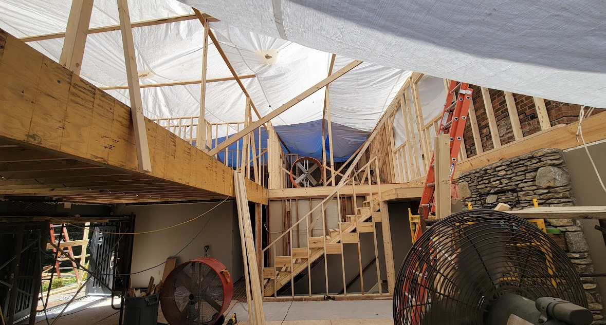 Partially built interior with wooden framing, stairs, and a red ladder under a translucent roof tarp