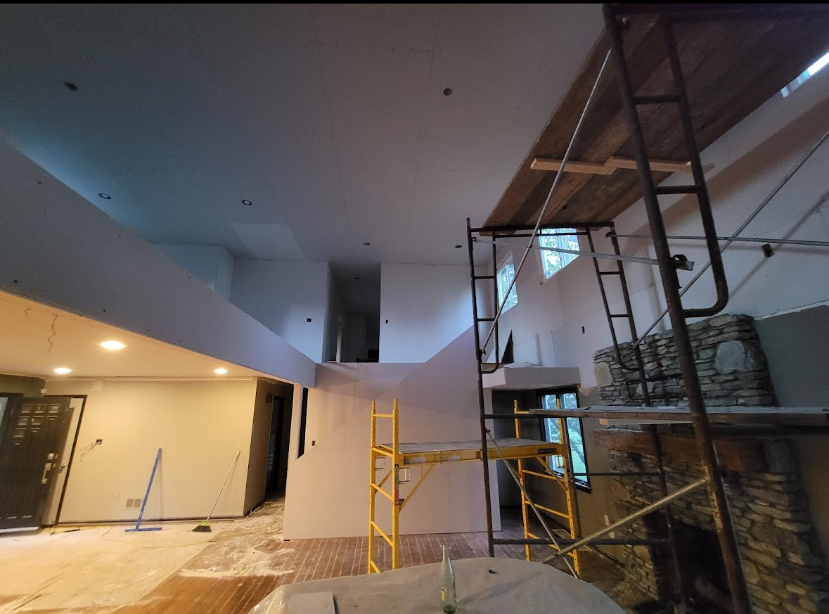 Interior under construction with scaffolding, ladders, and exposed walls beneath a high ceiling.