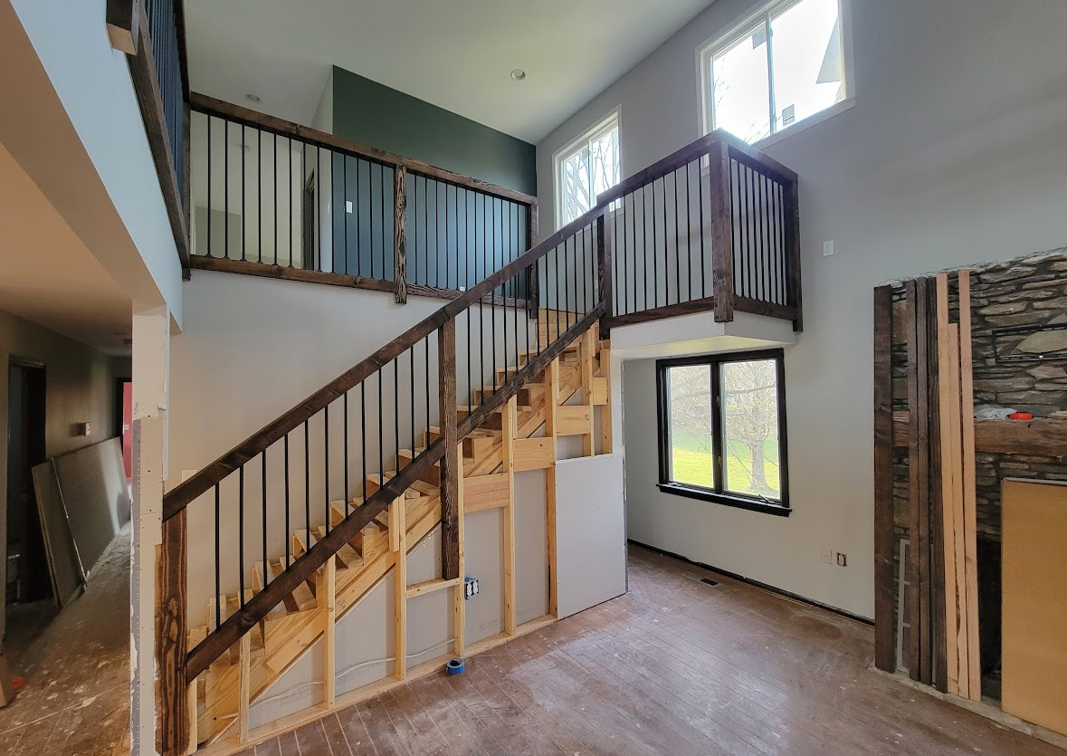 Interior with a staircase, loft railing, tall windows, and unfinished walls in a bright room