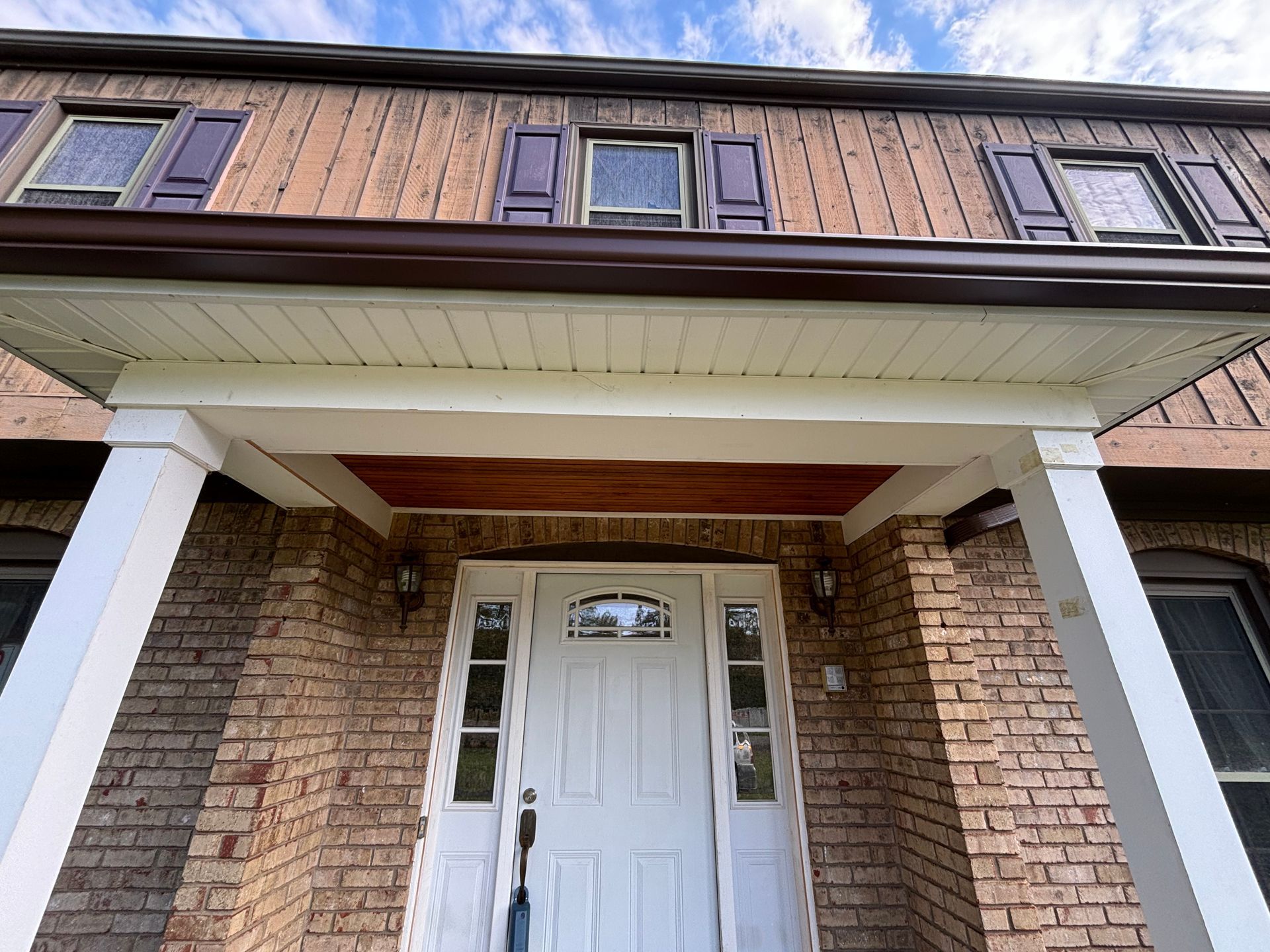 Front entrance of a brick townhouse with white columns and a white door under a covered porch