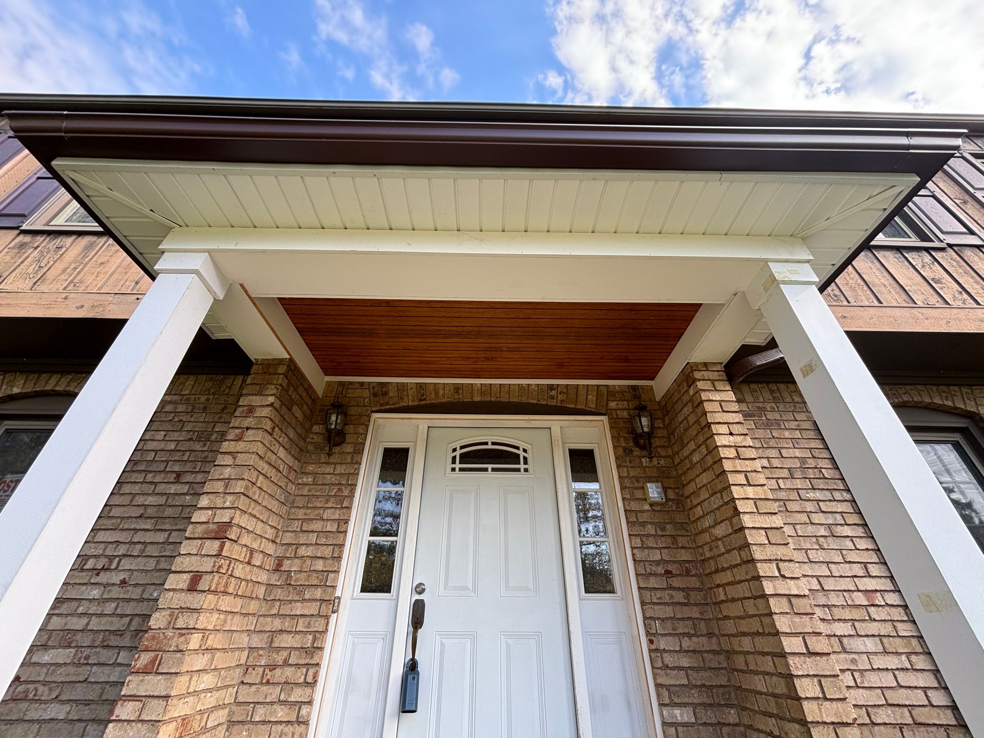 Front porch of a brick house with white columns, a white door, and a wood-paneled ceiling