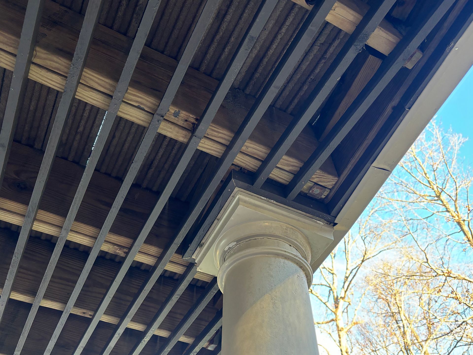 Underside of a bridge with steel beams and a white support column against a blue sky