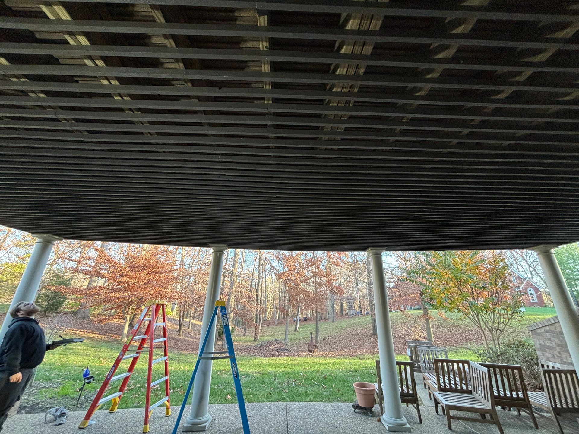 Covered playground pavilion with swings, a bench, and autumn trees in the background