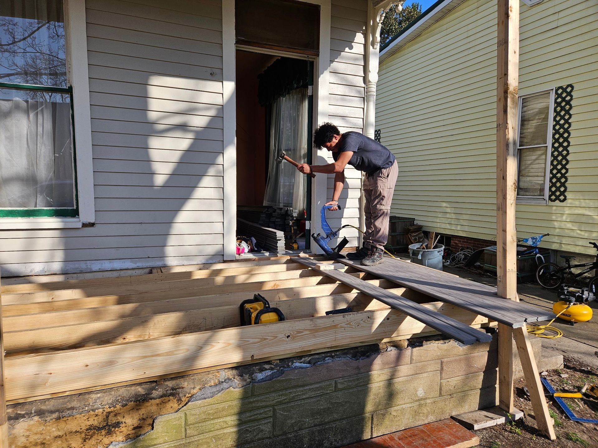 Person working on porch construction beside a house, with lumber and tools in the foreground