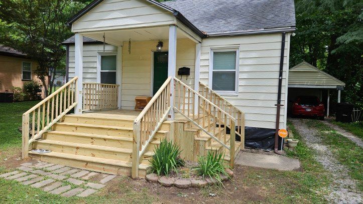 Small white house with front porch steps, green door, and a driveway with a carport beside it