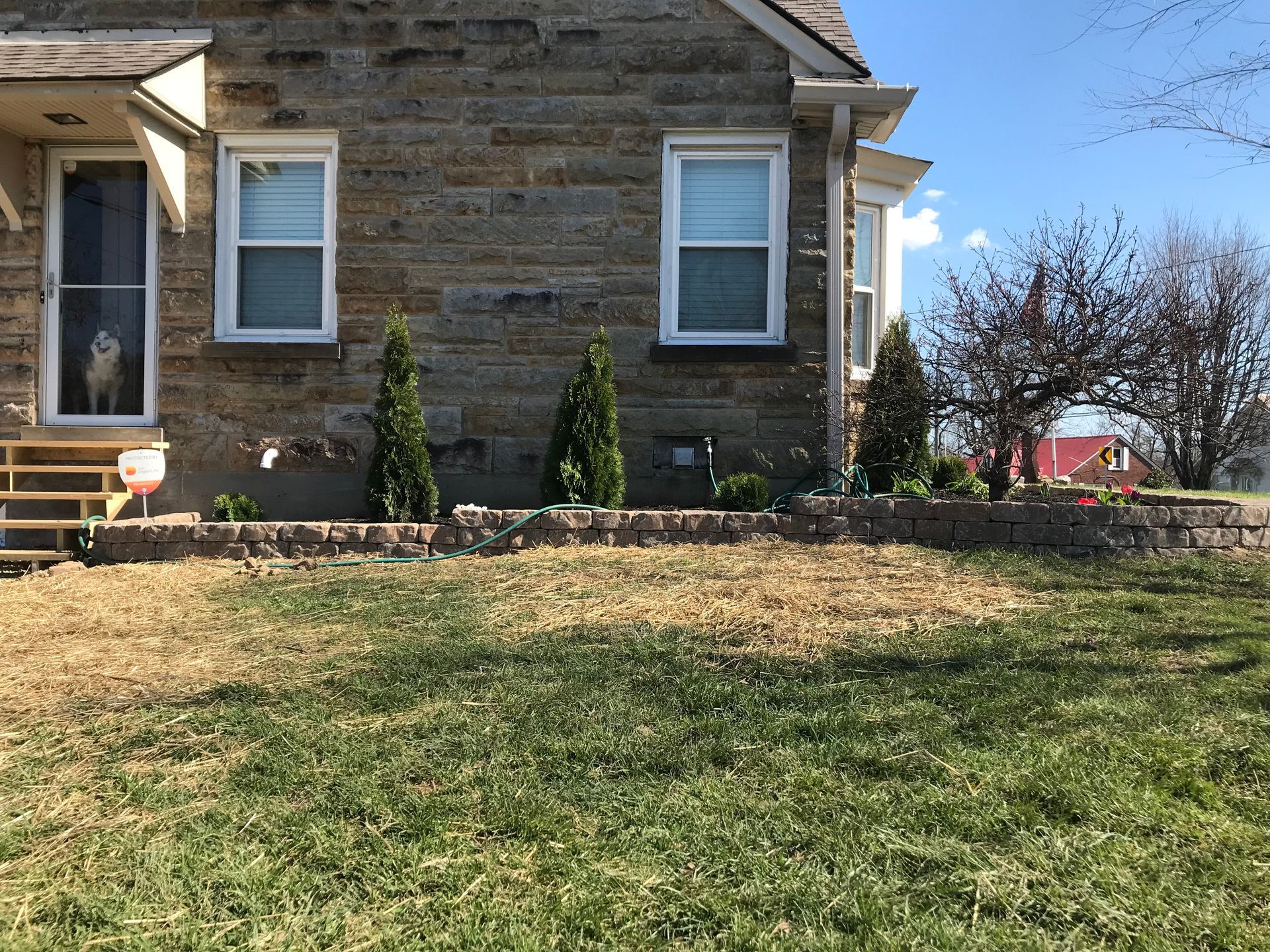Stone house exterior with two windows, a front bench, and a grassy yard under a clear blue sky