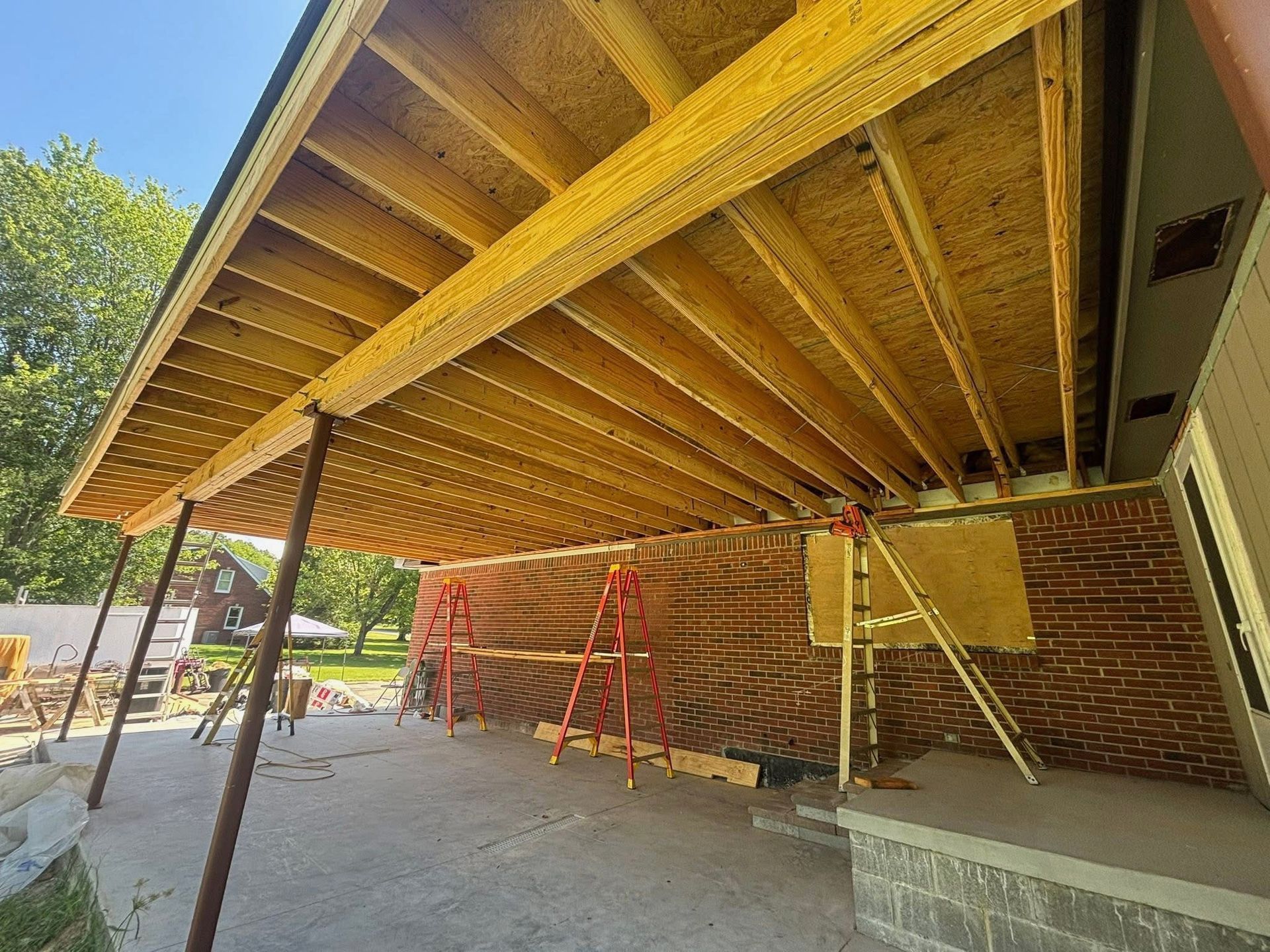 Under a building overhang, workers are repairing a wooden deck ceiling with scaffolding and ladders.