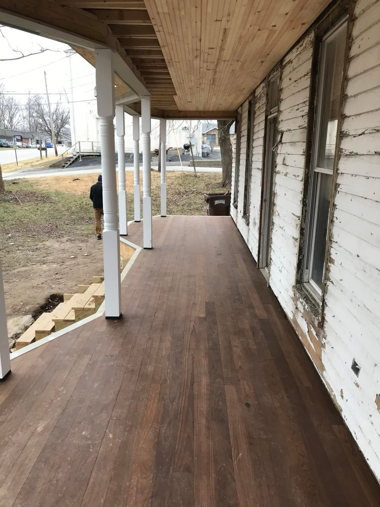 Covered wooden porch with white columns and peeling exterior wall beside a yard.