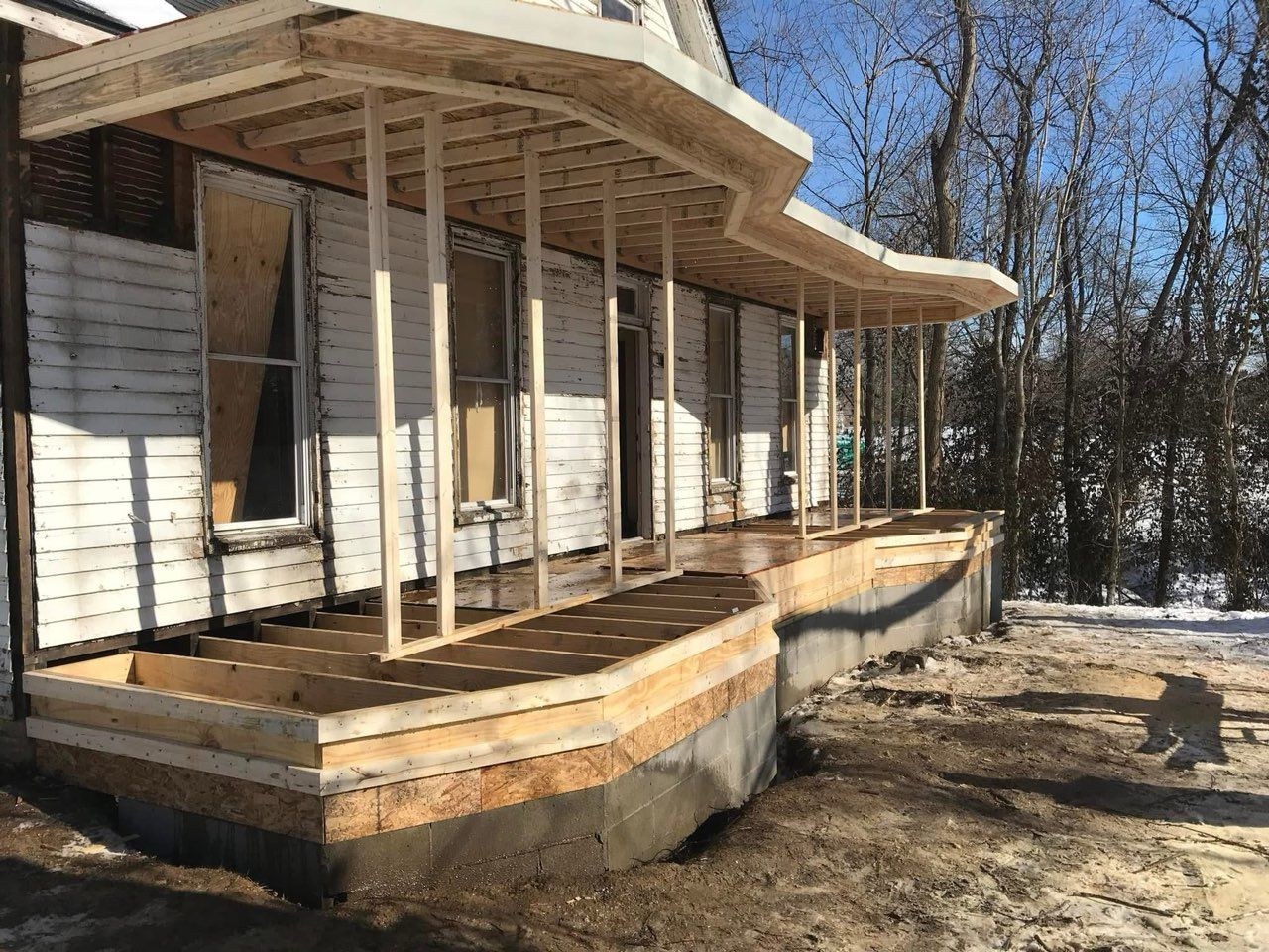 Old white house with a curved wooden porch and steps in a wooded yard