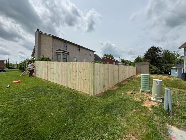 Wooden fence encloses a grassy yard beside a house under a cloudy sky