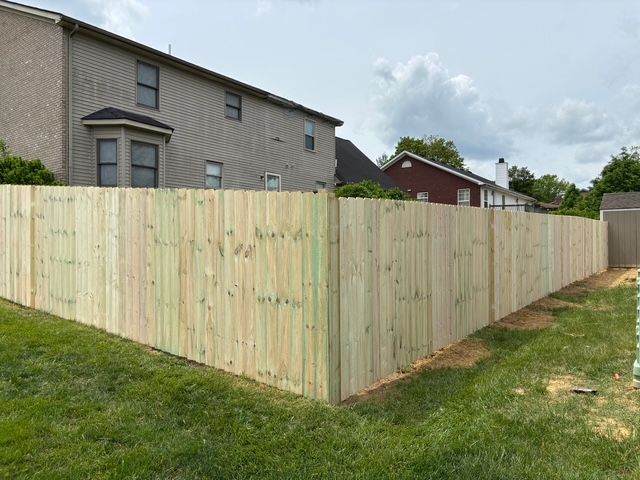 Light wood privacy fence enclosing a grassy yard beside a brick house under cloudy skies