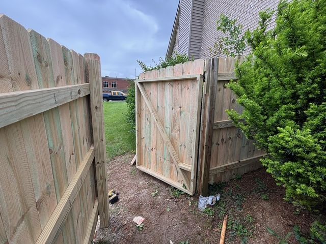 Open wooden gate in a backyard fence, with grass and a house in the background.