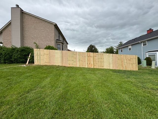 Backyard with a newly built wooden fence between two houses on a grassy hill under cloudy skies