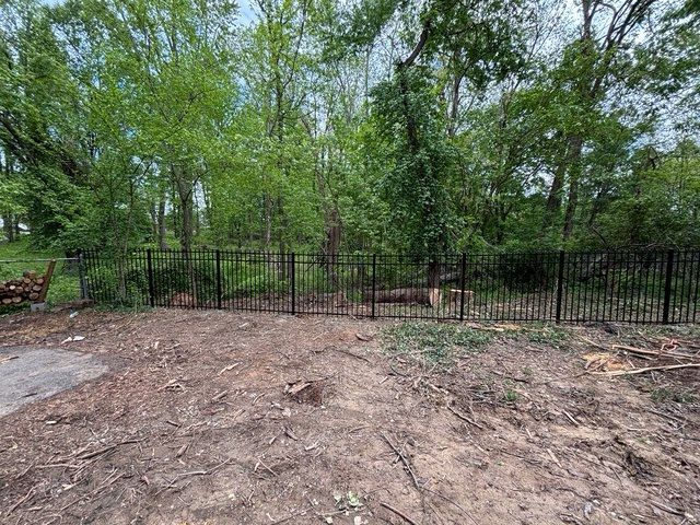 Bare dirt foreground with black metal fence and green trees in the background