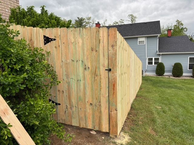 Wooden privacy fence panel beside a green hedge in a suburban backyard.